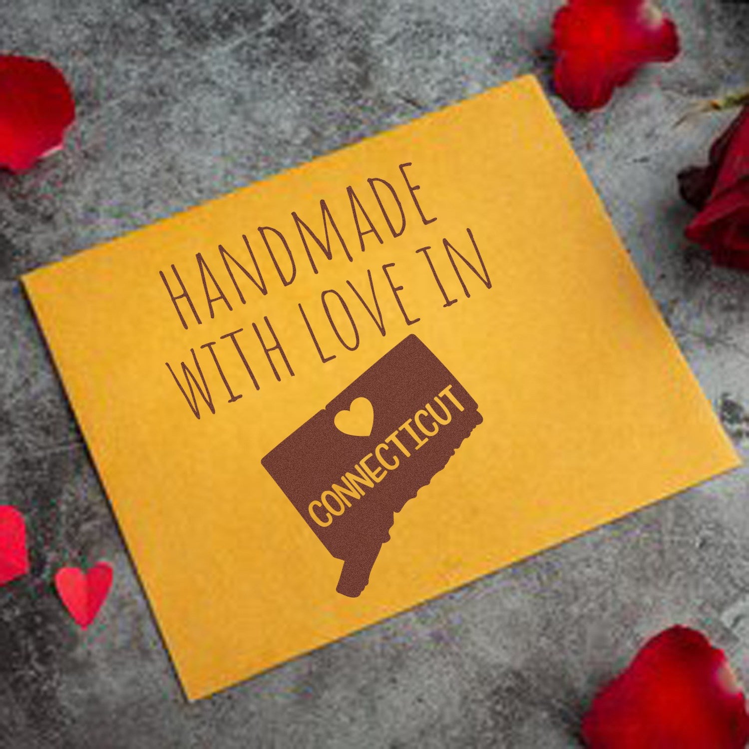 Wood Handle Connecticut Handmade with Love Rubber Stamp on a yellow envelope, featuring a heart and state outline, surrounded by red rose petals. Perfect for personalized crafts and gifts.