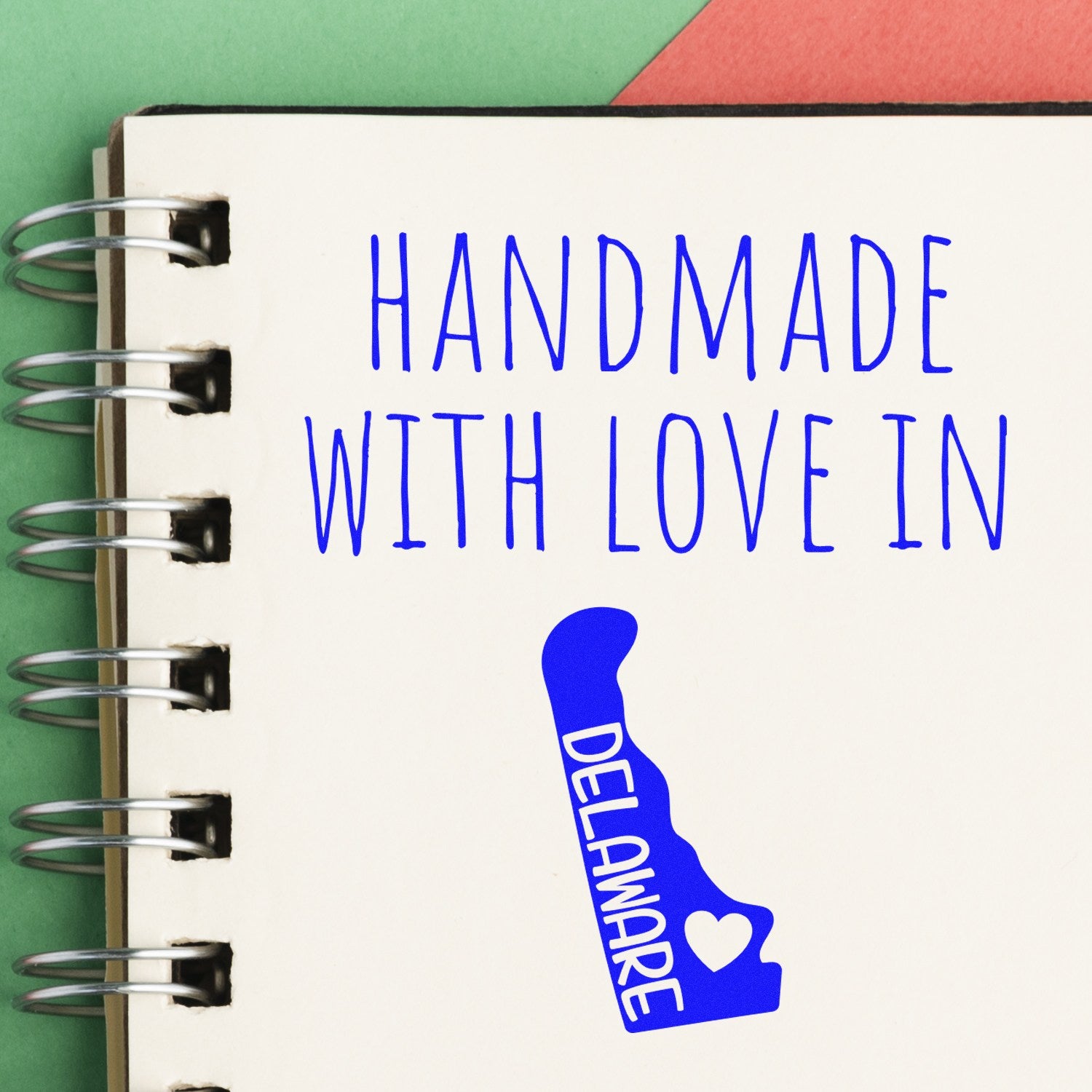 Wood Handle Delaware Handmade with Love Rubber Stamp on a notebook, featuring blue text and a Delaware state outline with a heart. Perfect for crafts and personalized projects.