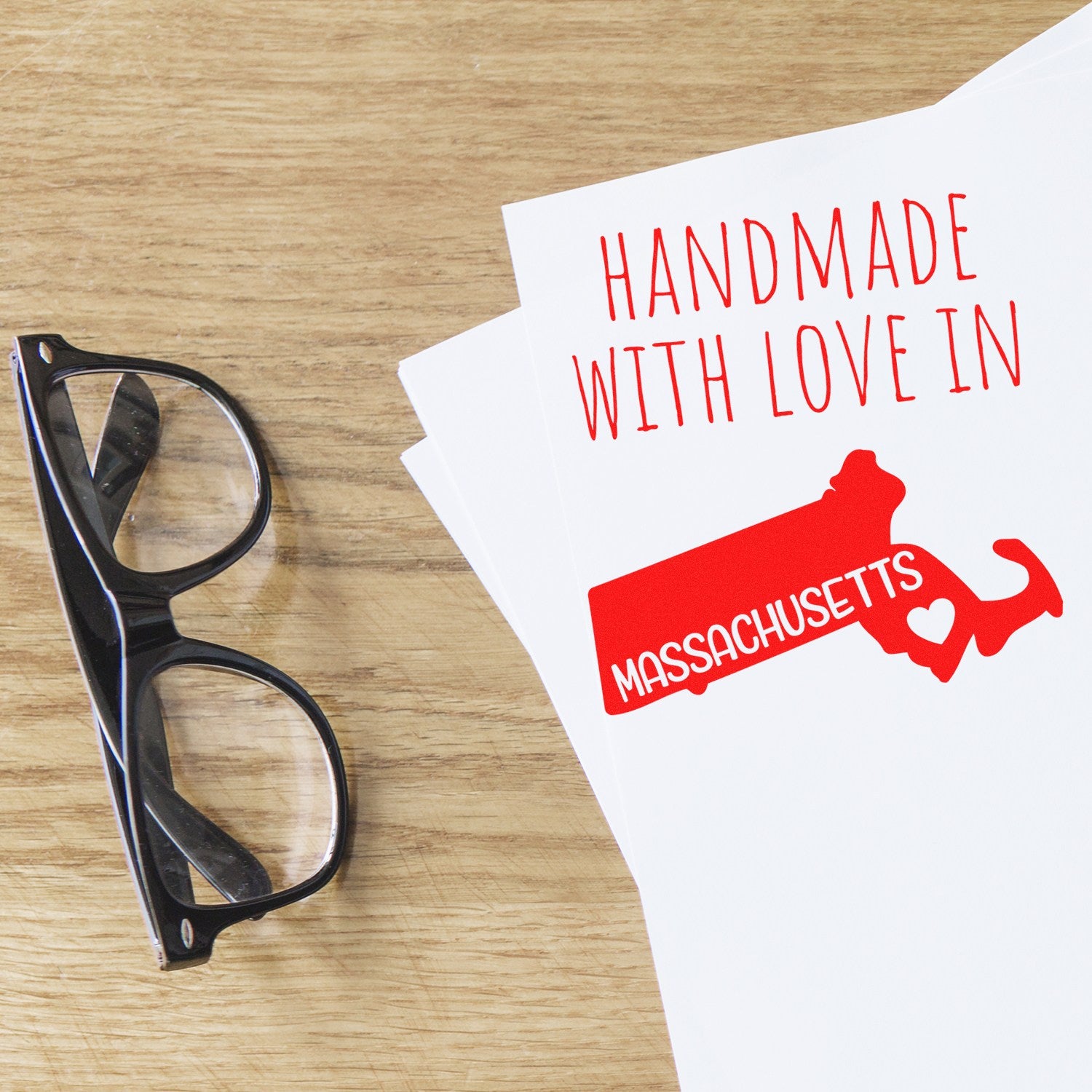 Wood Handle Massachusetts Handmade with Love Rubber Stamp on paper, featuring a red Massachusetts state outline with text, next to black glasses on a wooden surface.