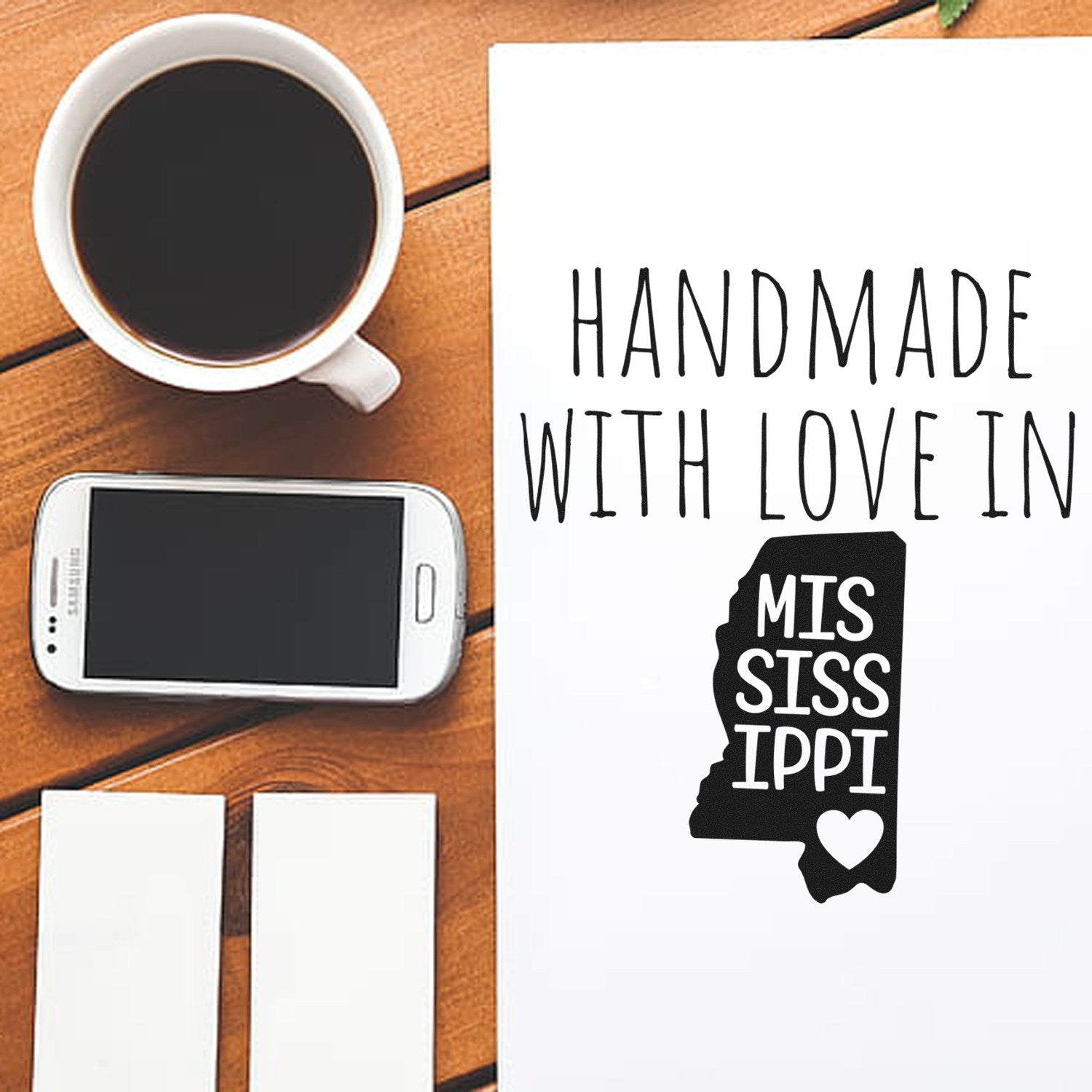 Handmade with Love in Mississippi Slim Pre-Inked Stamp on a wooden desk with a coffee cup, smartphone, and paper. Perfect for adding a personal touch to crafts and letters.