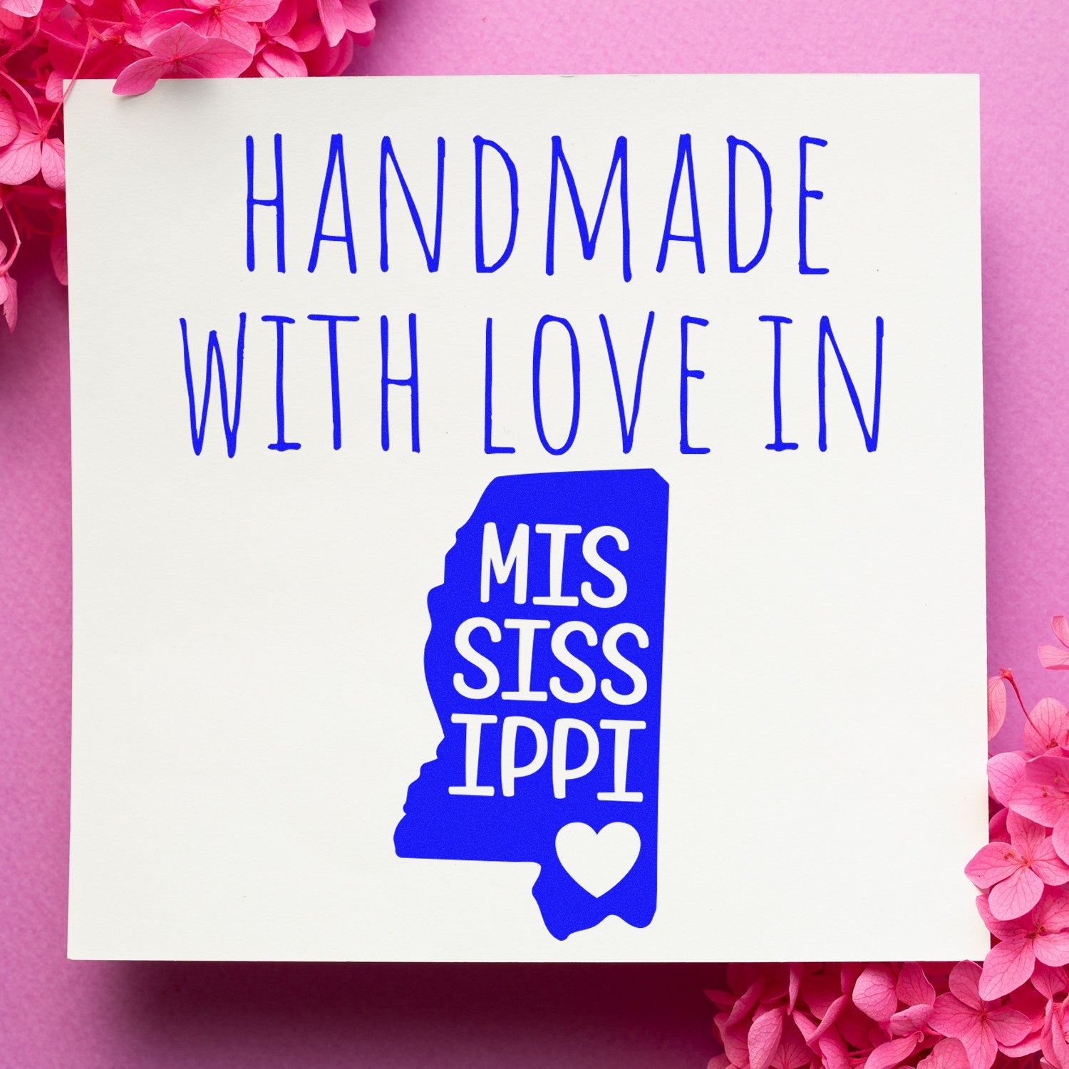 PSI Pre-Inked Handmade with Love in Mississippi stamp on pink background with floral accents, featuring blue text and state outline design.