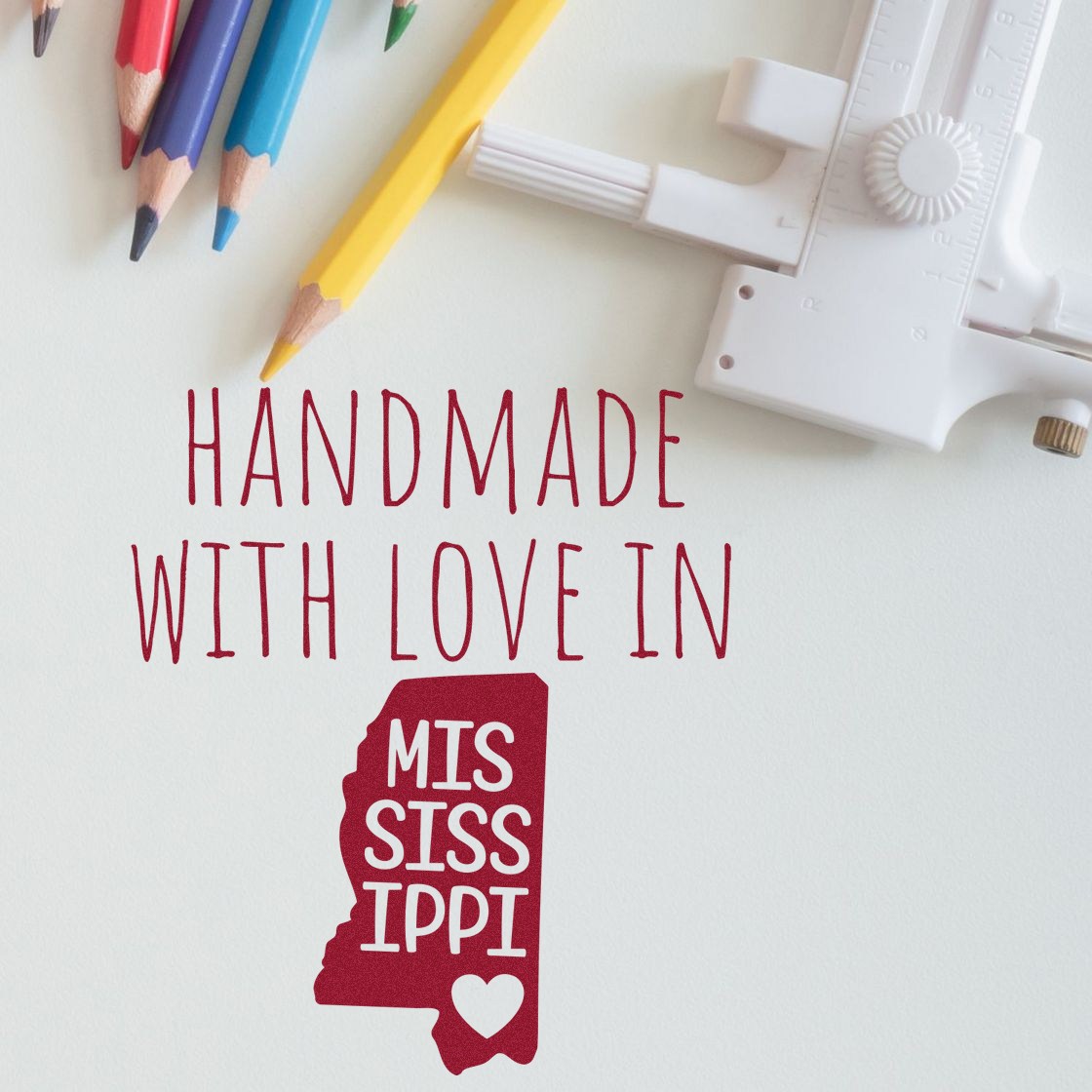 Wood Handle Mississippi Handmade with Love Rubber Stamp featuring a red Mississippi state outline with 'Handmade with Love' text, surrounded by colorful pencils and a ruler.