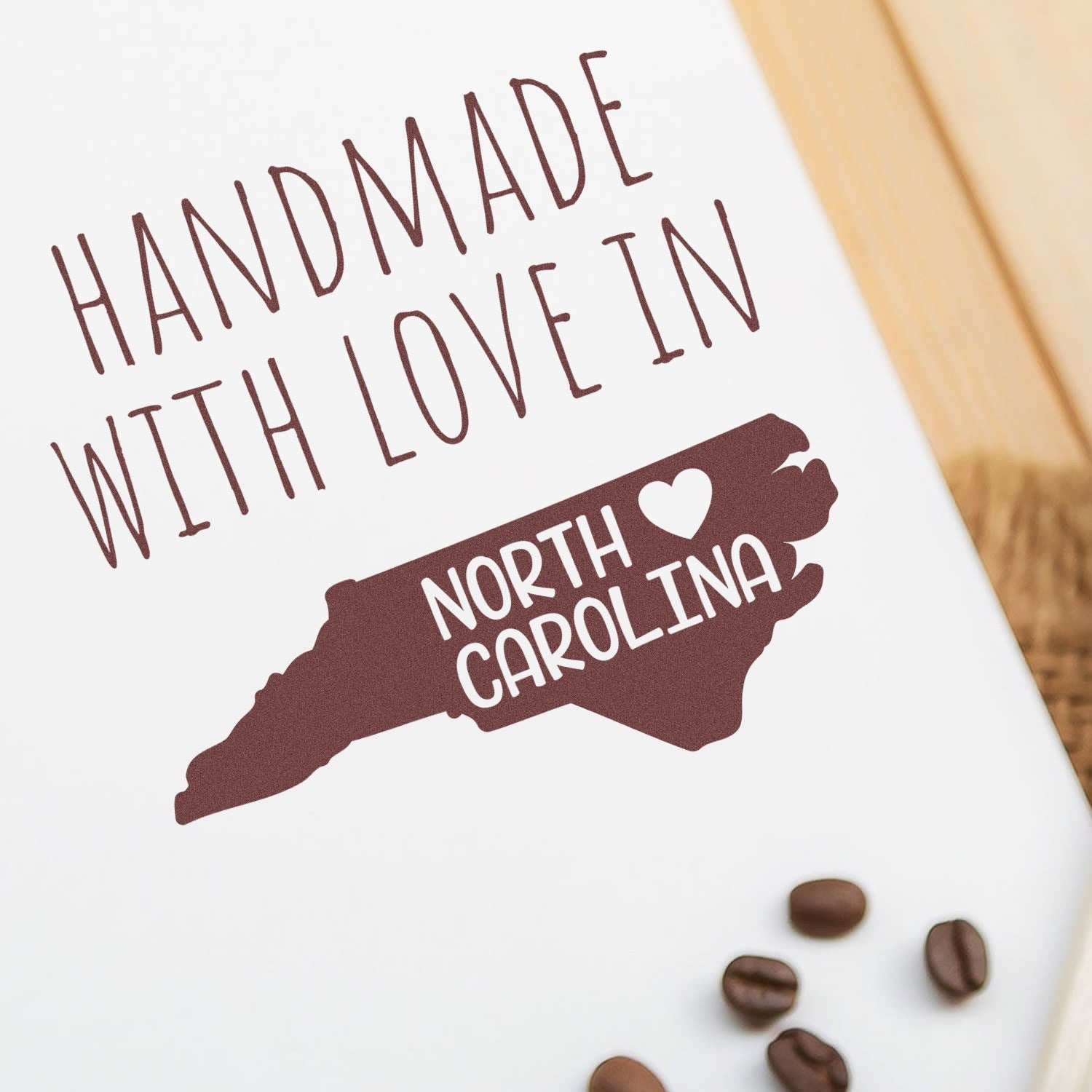 Handmade with Love in North Carolina Slim Pre-Inked Stamp featuring a North Carolina state outline with heart, displayed on a white surface with coffee beans.