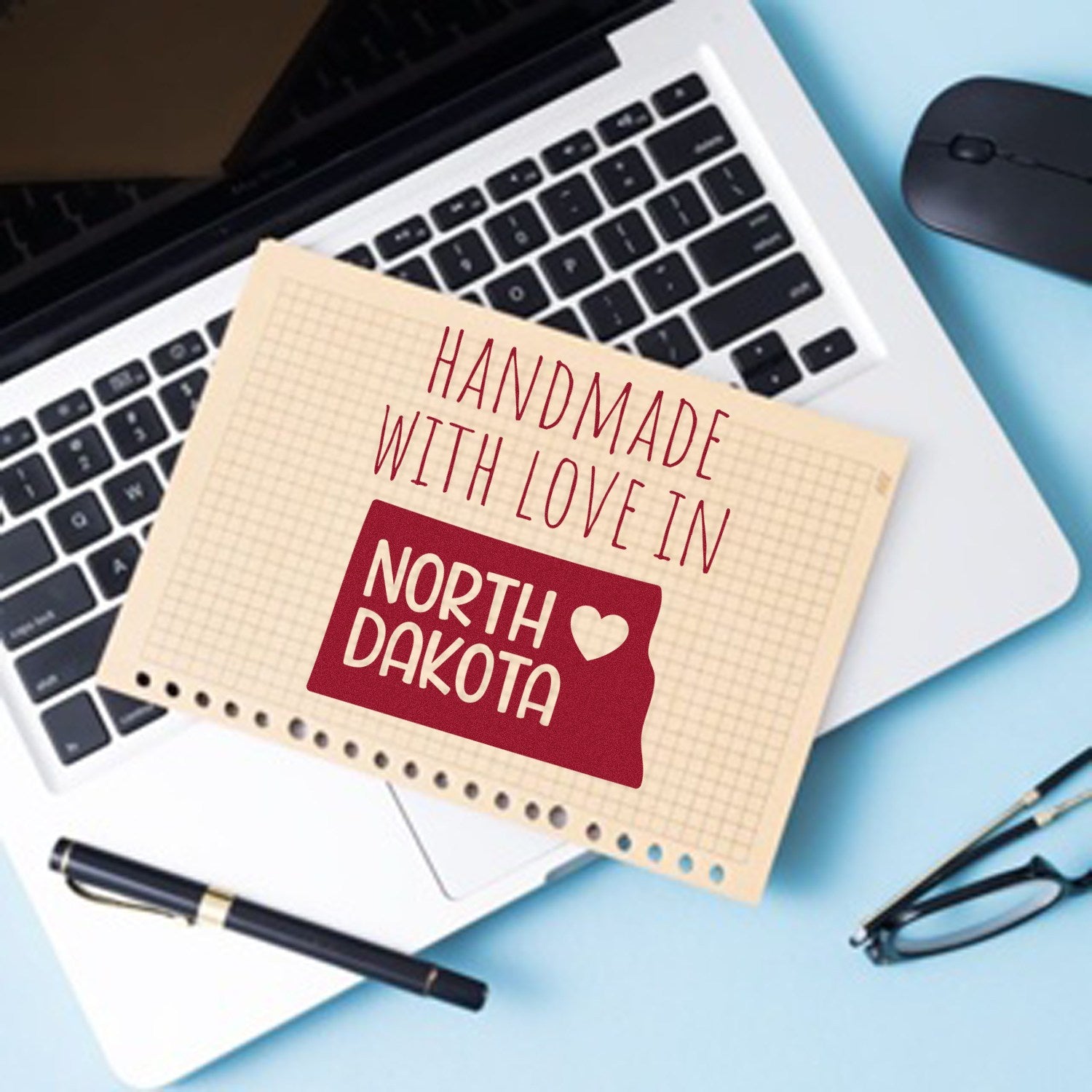 Self-Inking North Dakota Handmade with Love Stamp on a notepad, featuring a red state outline and heart, placed on a laptop keyboard.