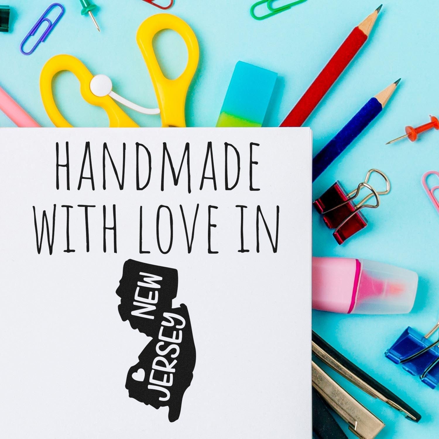 Self-Inking New Jersey Handmade with Love Stamp on paper, surrounded by colorful stationery, featuring a heart design within the state outline. Perfect for crafts and personalized projects.