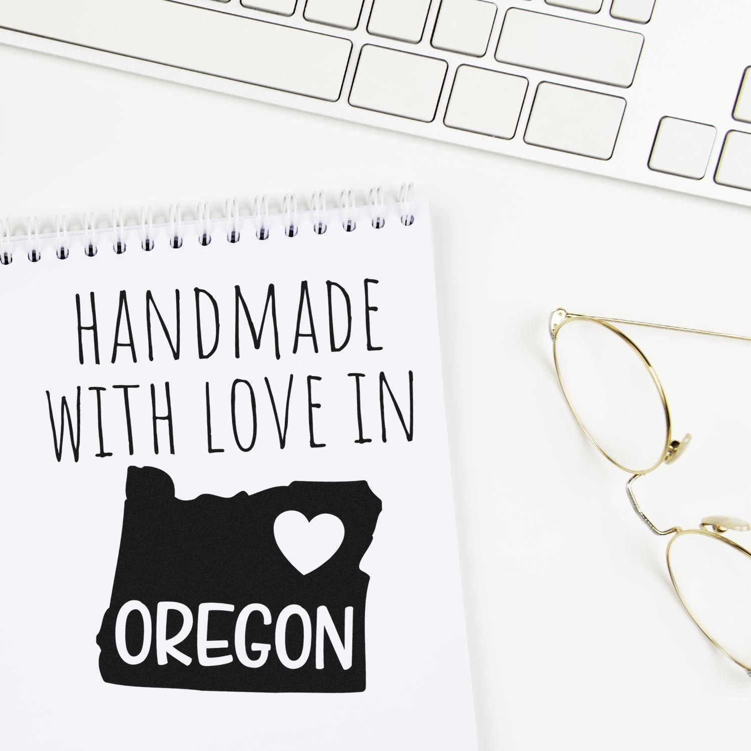 Handmade with Love in Oregon Slim Pre-Inked Stamp on notepad, featuring Oregon state outline and heart, next to a keyboard and glasses.