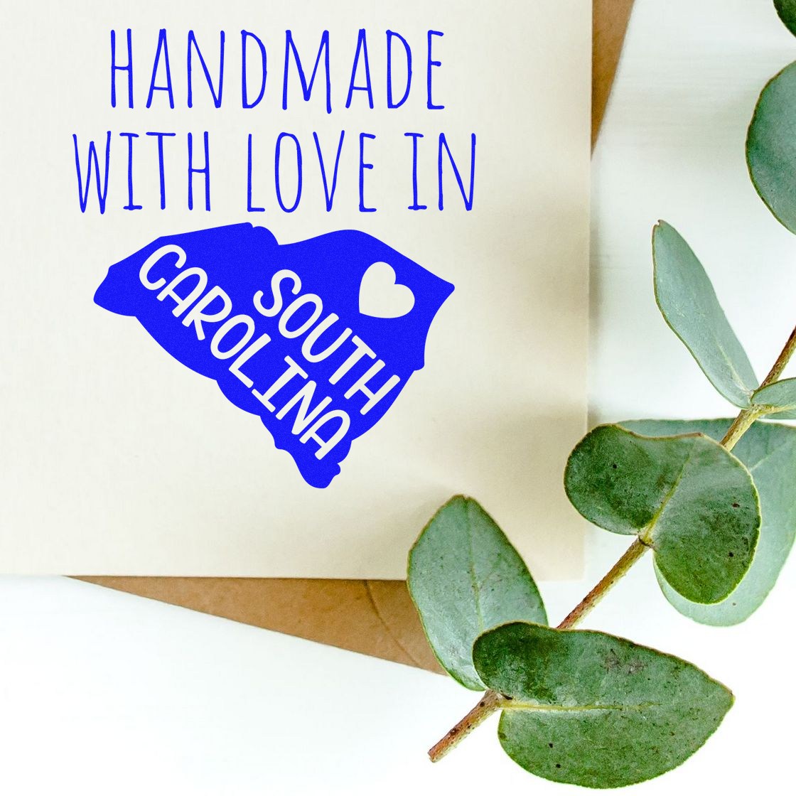 Wood Handle South Carolina Handmade with Love Rubber Stamp on a card with green leaves, featuring a blue design of South Carolina and a heart. Perfect for crafts and personalized gifts.