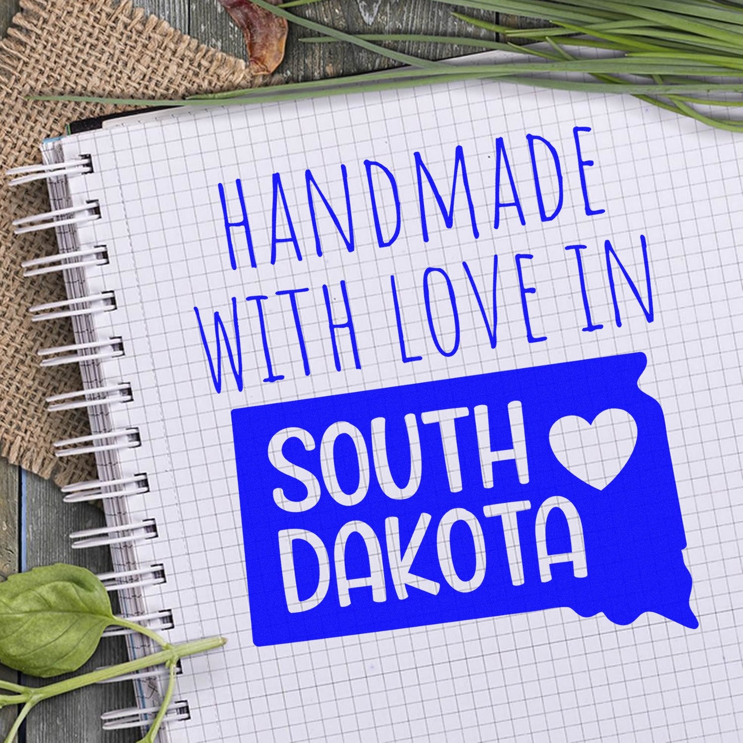 Handmade with Love in South Dakota Slim Pre-Inked Stamp on a notebook, featuring blue text and a heart design on a state outline.