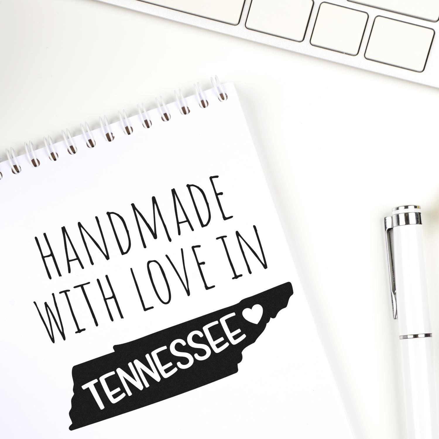 Handmade with Love in Tennessee Slim Pre-Inked Stamp on notepad, featuring a black Tennessee state outline with a heart, next to a white pen and keyboard. Perfect for crafts and gifts.