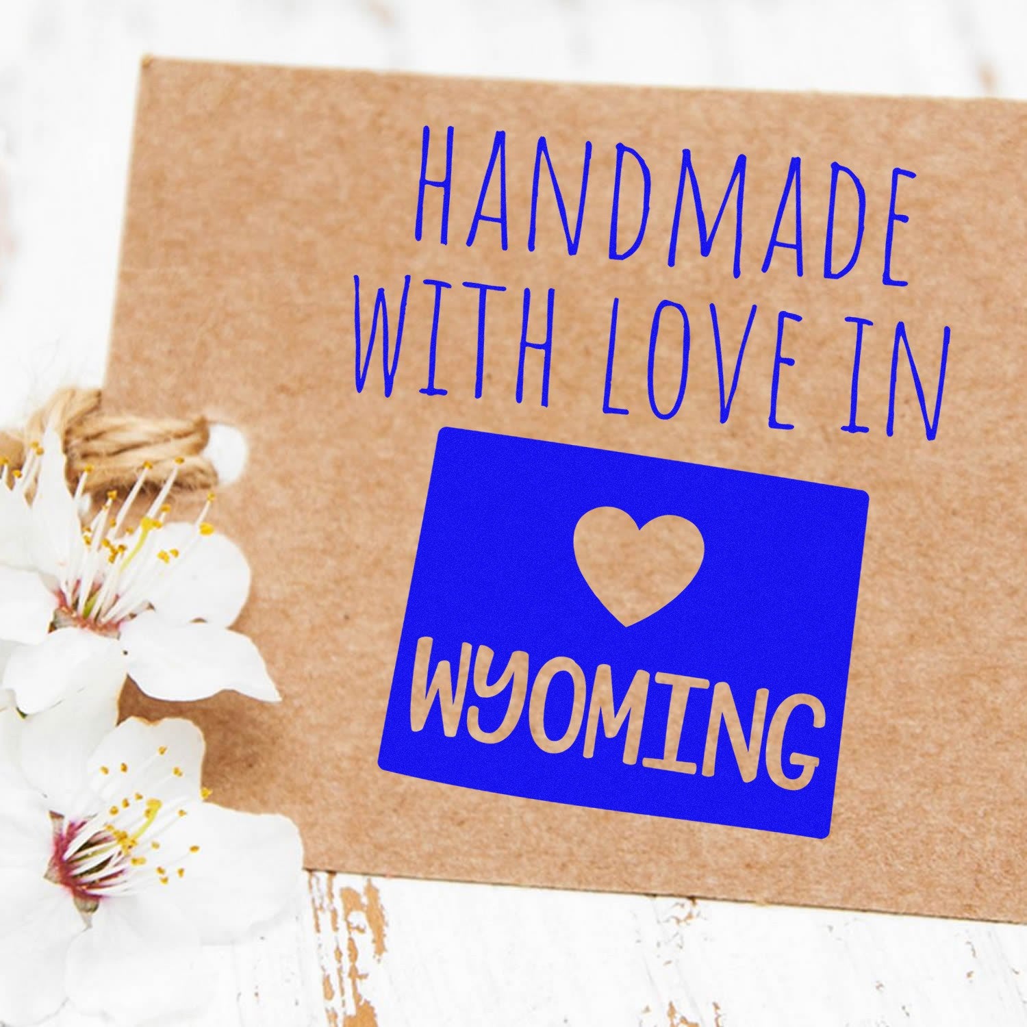 Self-Inking Wyoming Handmade with Love Stamp on a brown card with blue text and heart design, surrounded by white flowers. Perfect for crafts and gifts.