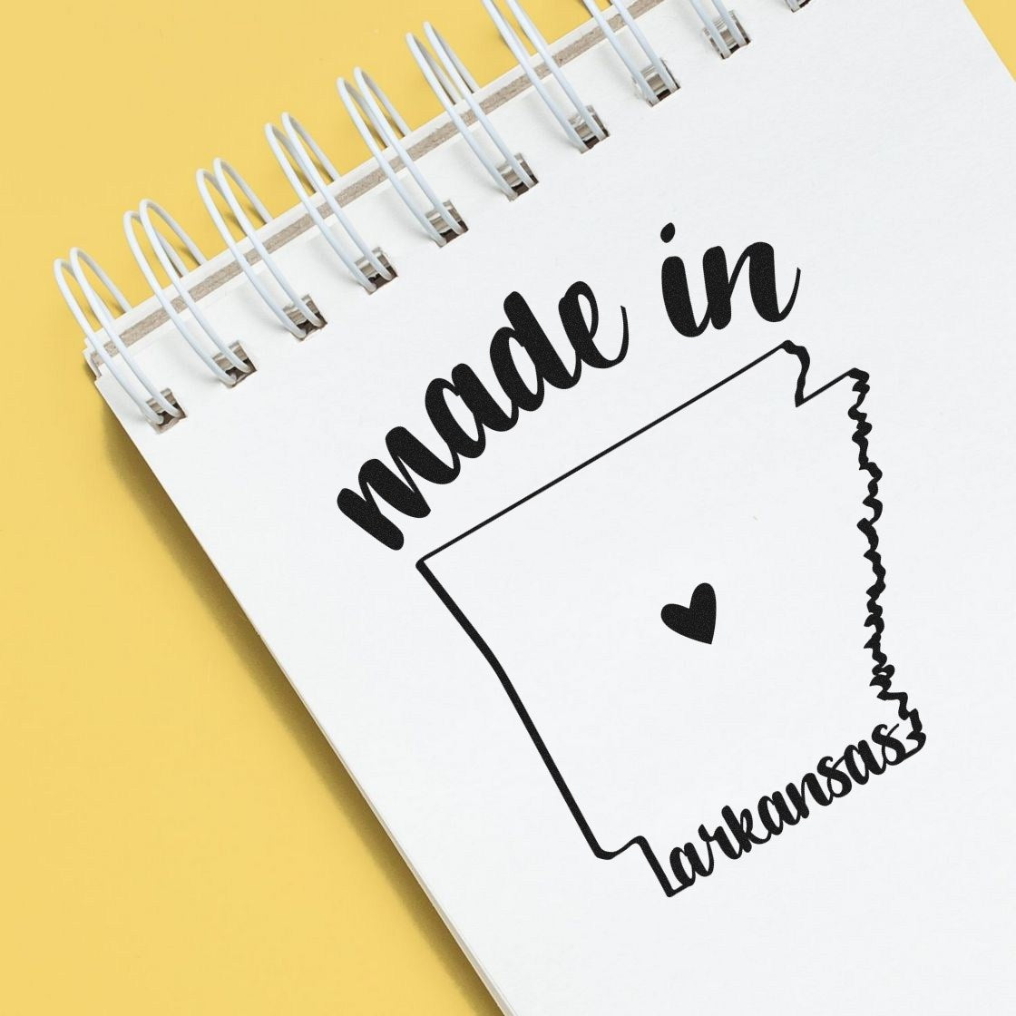 Made with Love in Arkansas Rubber Stamp featuring a heart inside the state outline, stamped on a notebook page. Perfect for crafts and gifts. Black ink on white paper.