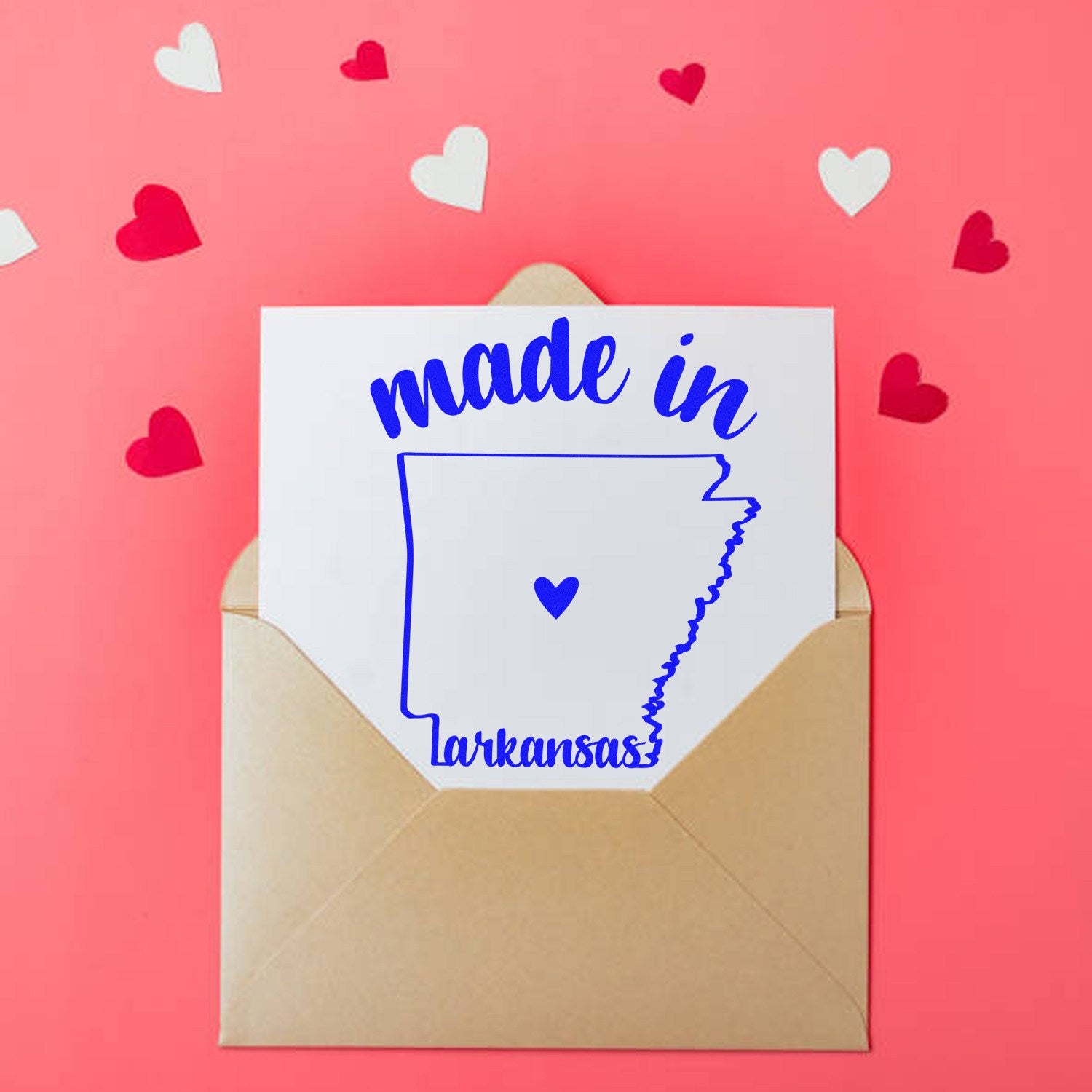 Made with Love in Arkansas Rubber Stamp on a card in a kraft envelope, surrounded by red and white heart cutouts on a pink background.