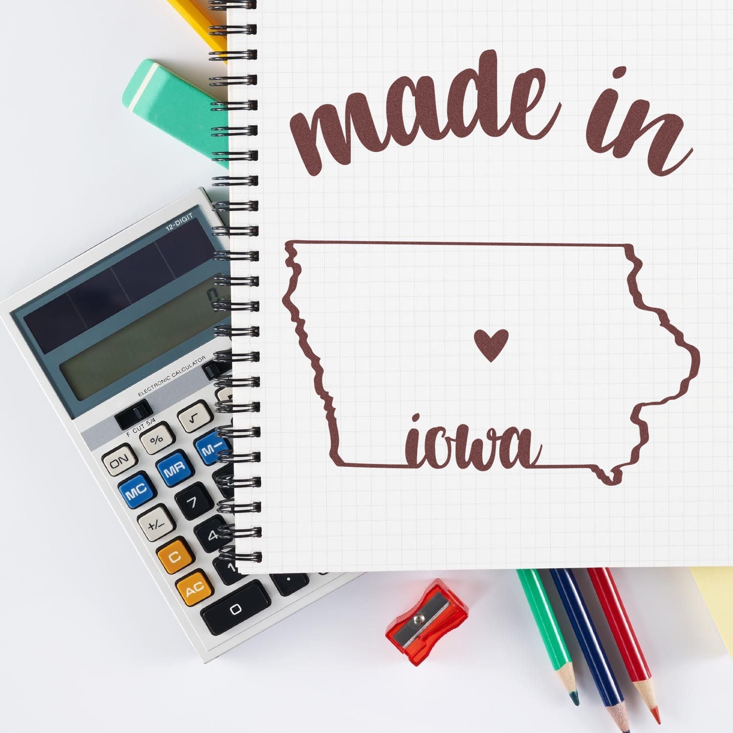 Self-Inking Handmade with Love in Iowa Stamp on a notebook with a map of Iowa and heart design, surrounded by colorful stationery and a calculator.