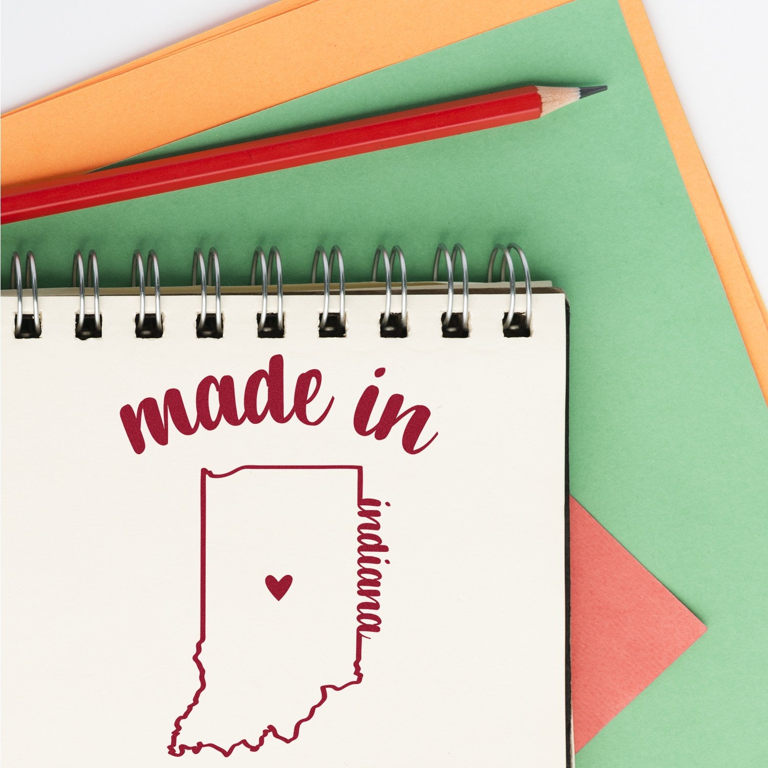 Made with Love in Indiana Rubber Stamp featuring a heart inside the state outline, displayed on a notepad with colorful paper and a red pencil.