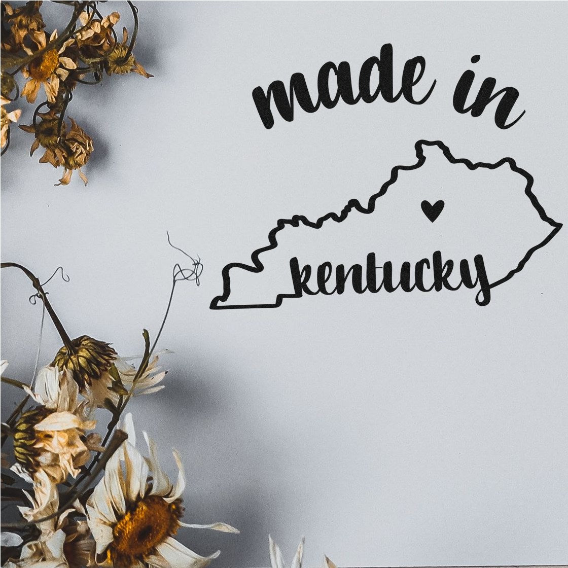 Image of Slim Pre-Inked Stamp Kentucky Made in Stamp, featuring a black outline of Kentucky with made in kentucky text, surrounded by dried flowers on a light background.