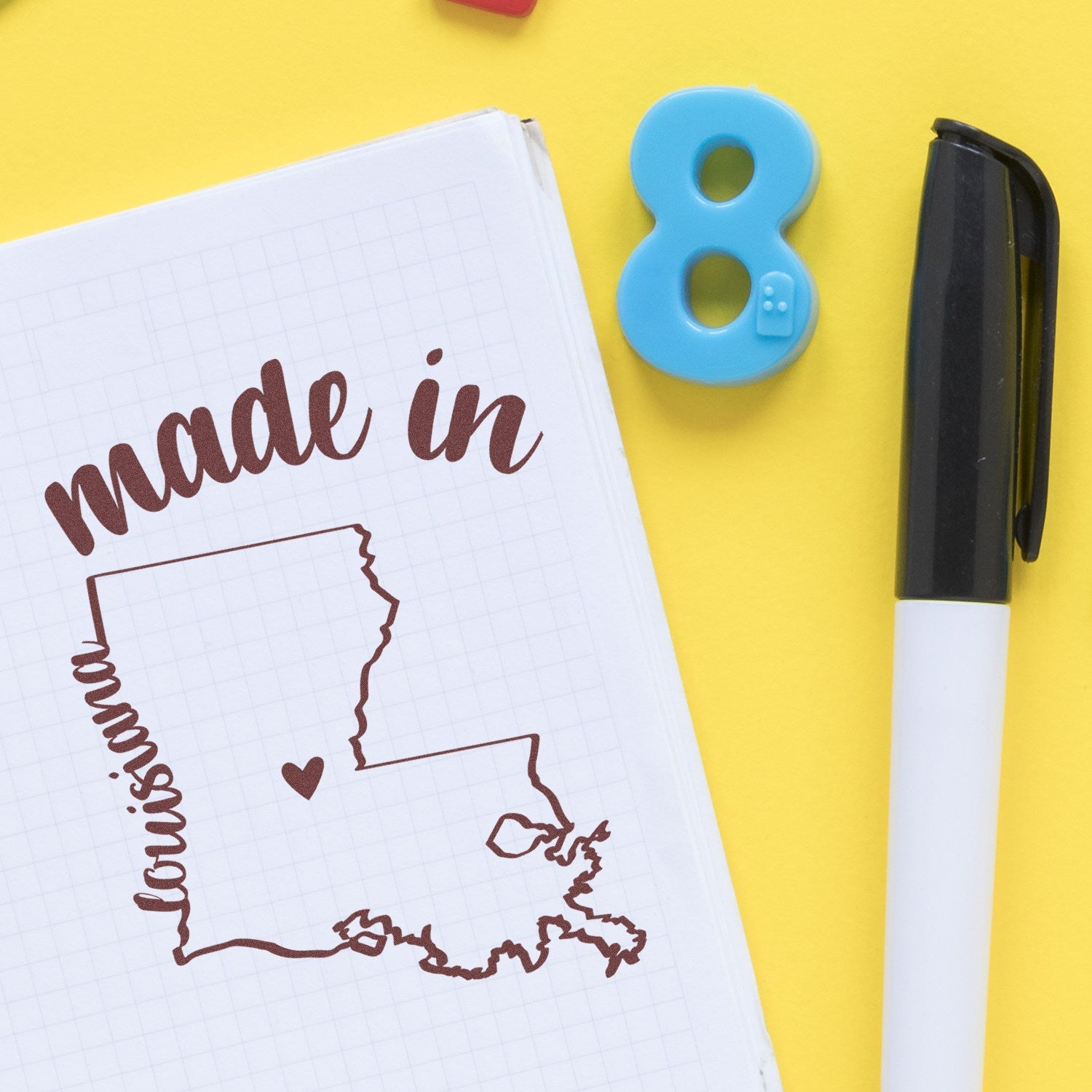 Made in Louisiana Stamp Pre-Inked featuring a map outline with 'made in' text, displayed on a notepad with a pen and number 8 eraser on a yellow background.