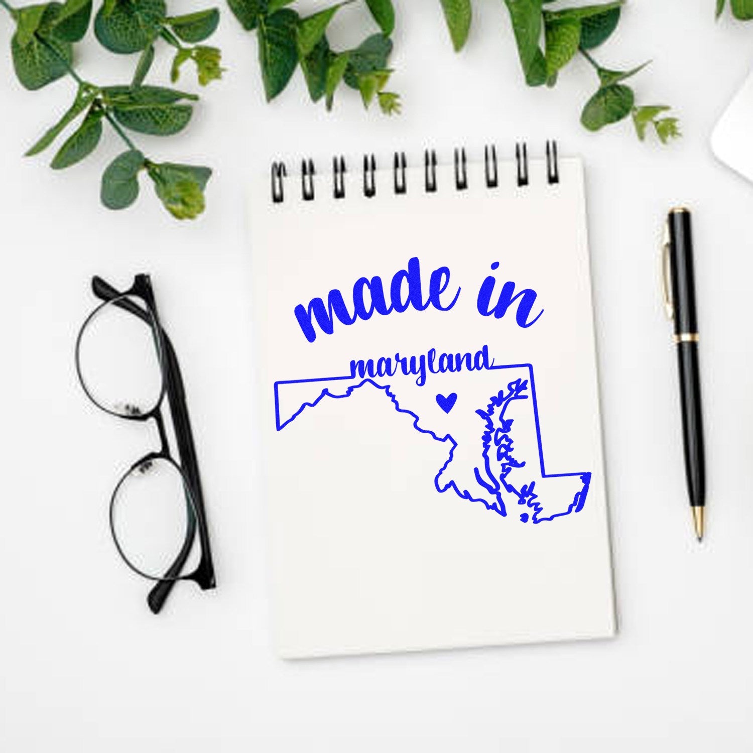 Made with Love in Maryland Rubber Stamp featuring a blue outline of Maryland with 'made in maryland' text, displayed on a notepad with glasses and a pen nearby.