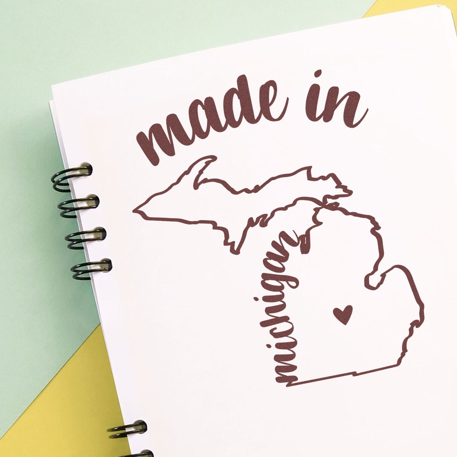 Self-Inking Handmade with Love in Michigan Stamp featuring a map outline of Michigan with 'made in' text, perfect for crafts and gifts. Compact design on a spiral notebook.