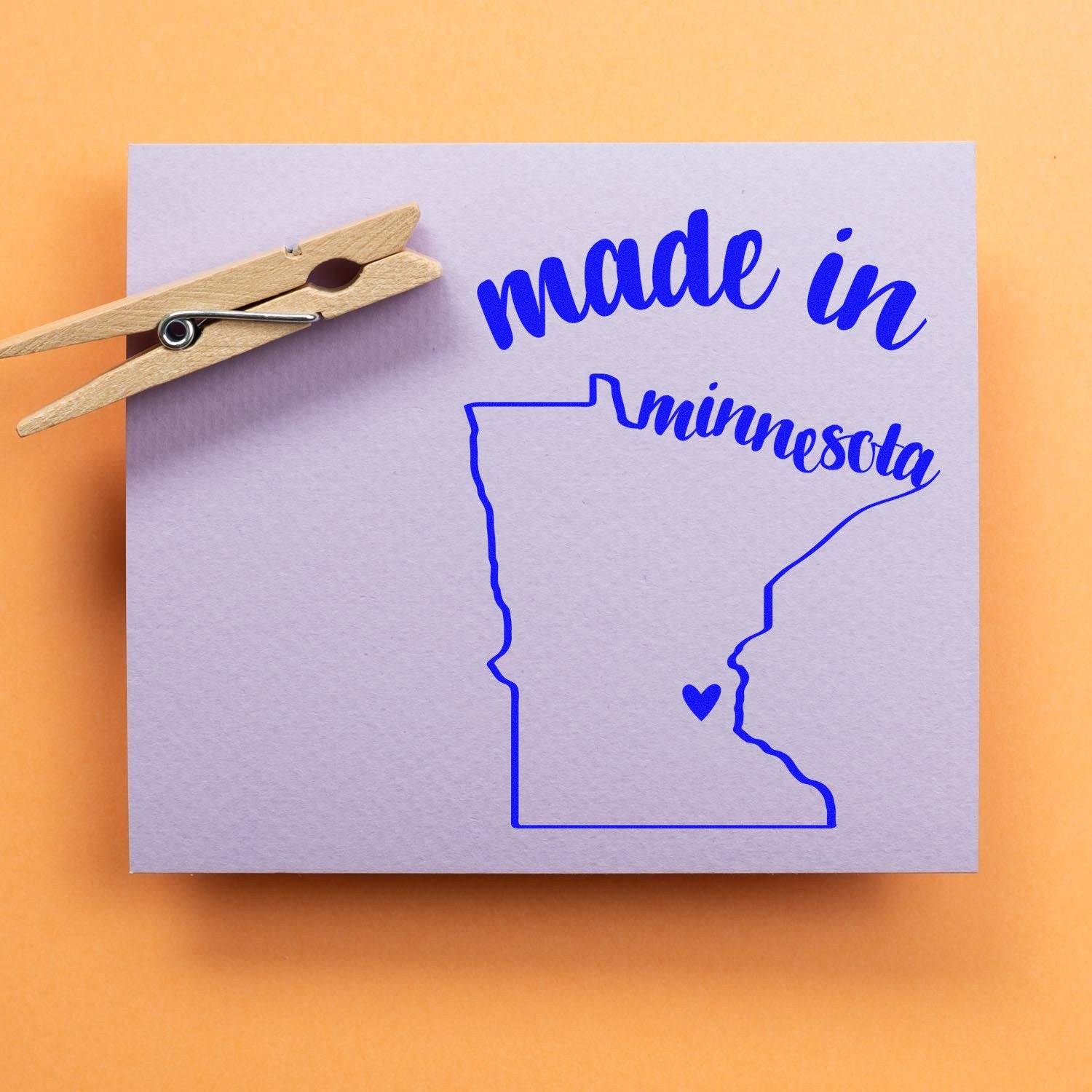 Self-Inking Handmade with Love in Minnesota Stamp on a purple card with a blue outline of Minnesota and a heart, accompanied by a wooden clothespin.