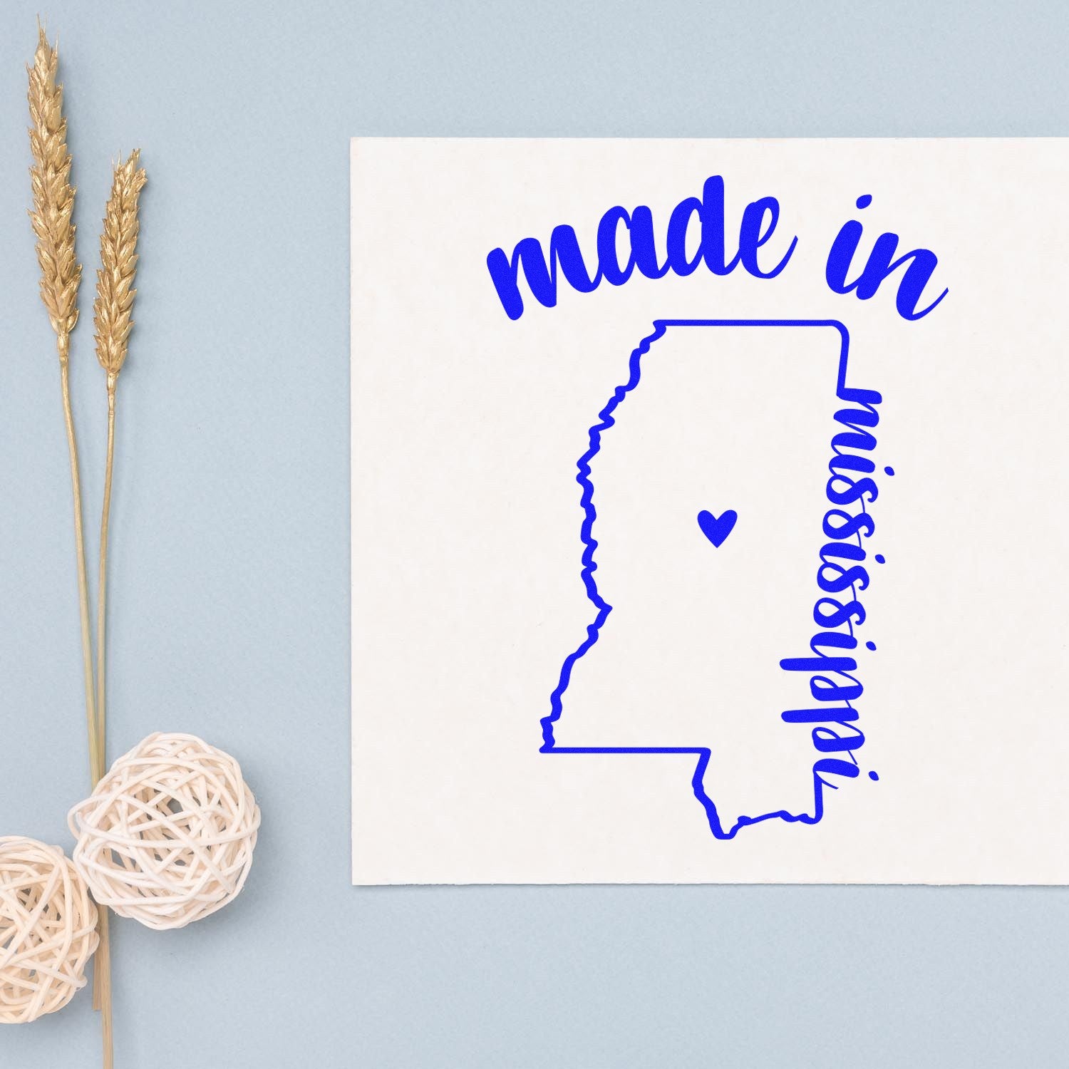 Made in Mississippi Stamp Pre-Inked: Blue stamp design featuring the outline of Mississippi with a heart, and 'made in' text, on a light background with decorative elements.