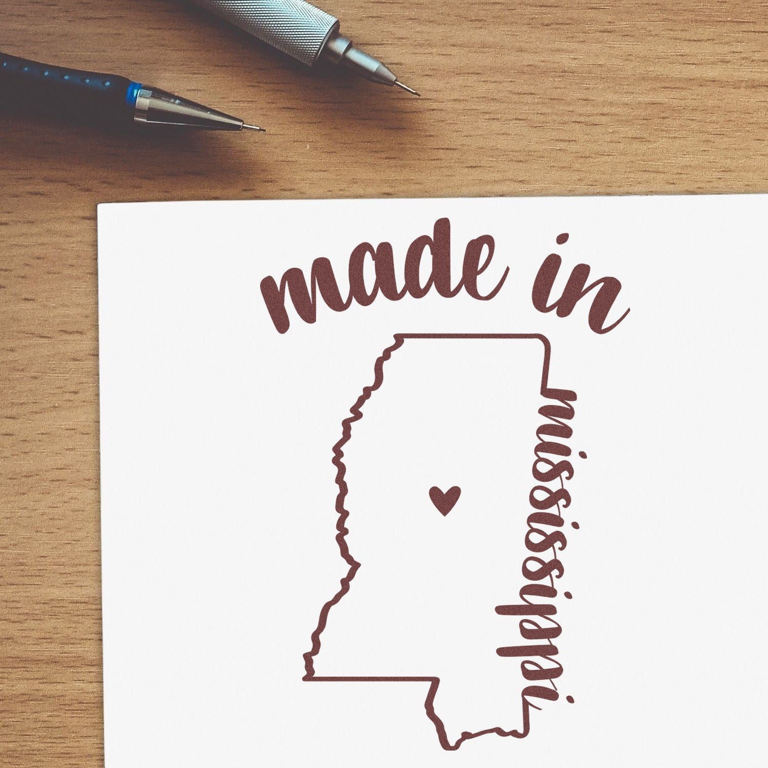 Self-Inking Handmade with Love in Mississippi Stamp featuring a heart and state outline on paper, with pens nearby. Perfect for crafts and personalized projects.