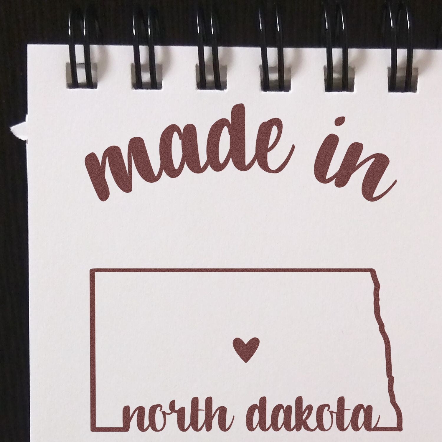 Slim Pre-Inked Stamp North Dakota Made in Stamp featuring a heart inside the state outline, with made in north dakota text on a spiral-bound notepad.