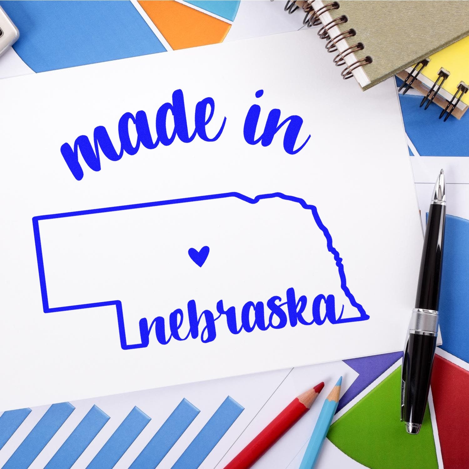 Self-Inking Handmade with Love in Nebraska Stamp featuring a blue outline of Nebraska with a heart, surrounded by colorful stationery and a pen.