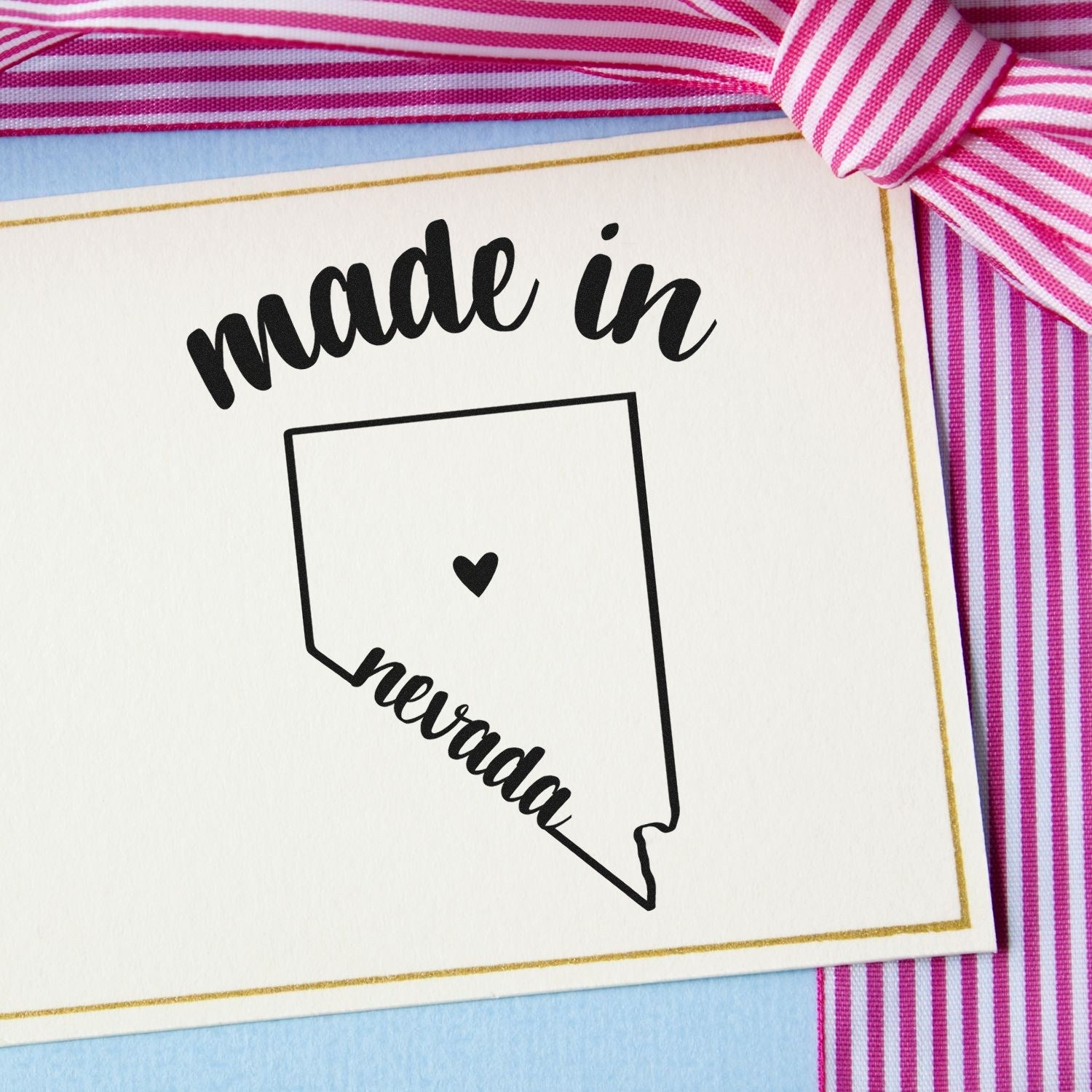 Made with Love in Nevada Rubber Stamp featuring a heart inside the Nevada state outline, displayed on a card with pink and white striped ribbon.