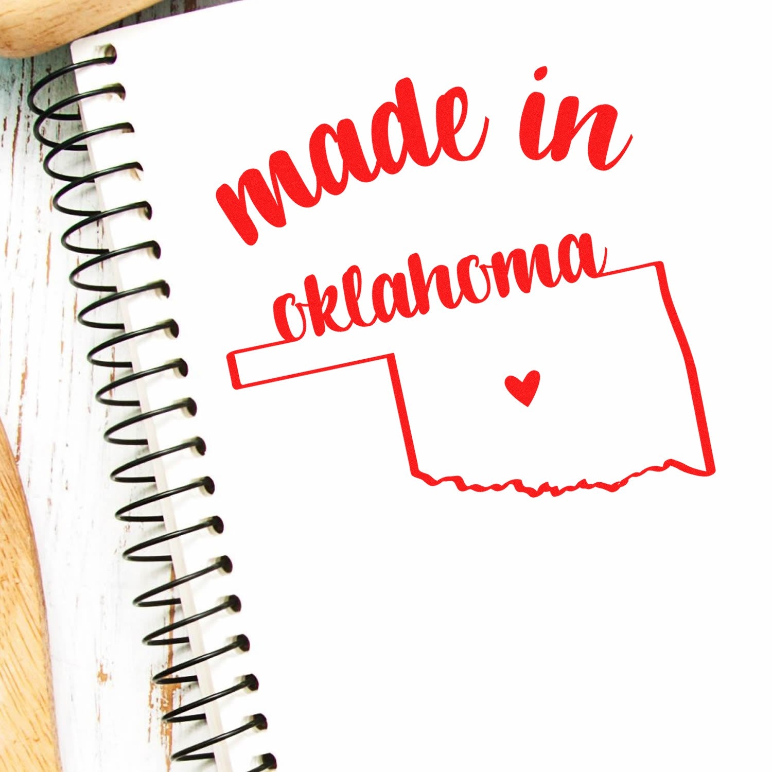 Self-Inking Handmade with Love in Oklahoma Stamp on a spiral notebook, featuring a red outline of Oklahoma with a heart, and the text made in oklahoma in bold red script.