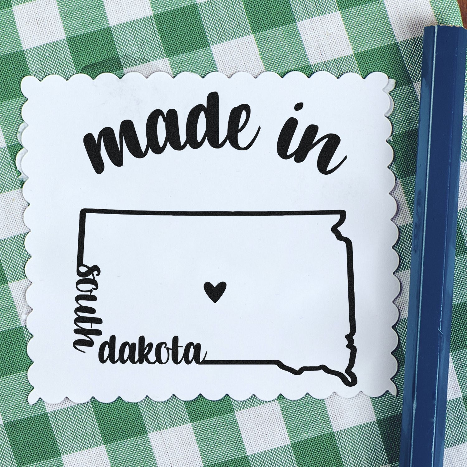 Made with Love in South Dakota Rubber Stamp featuring a heart inside the state outline, placed on a green checkered background.