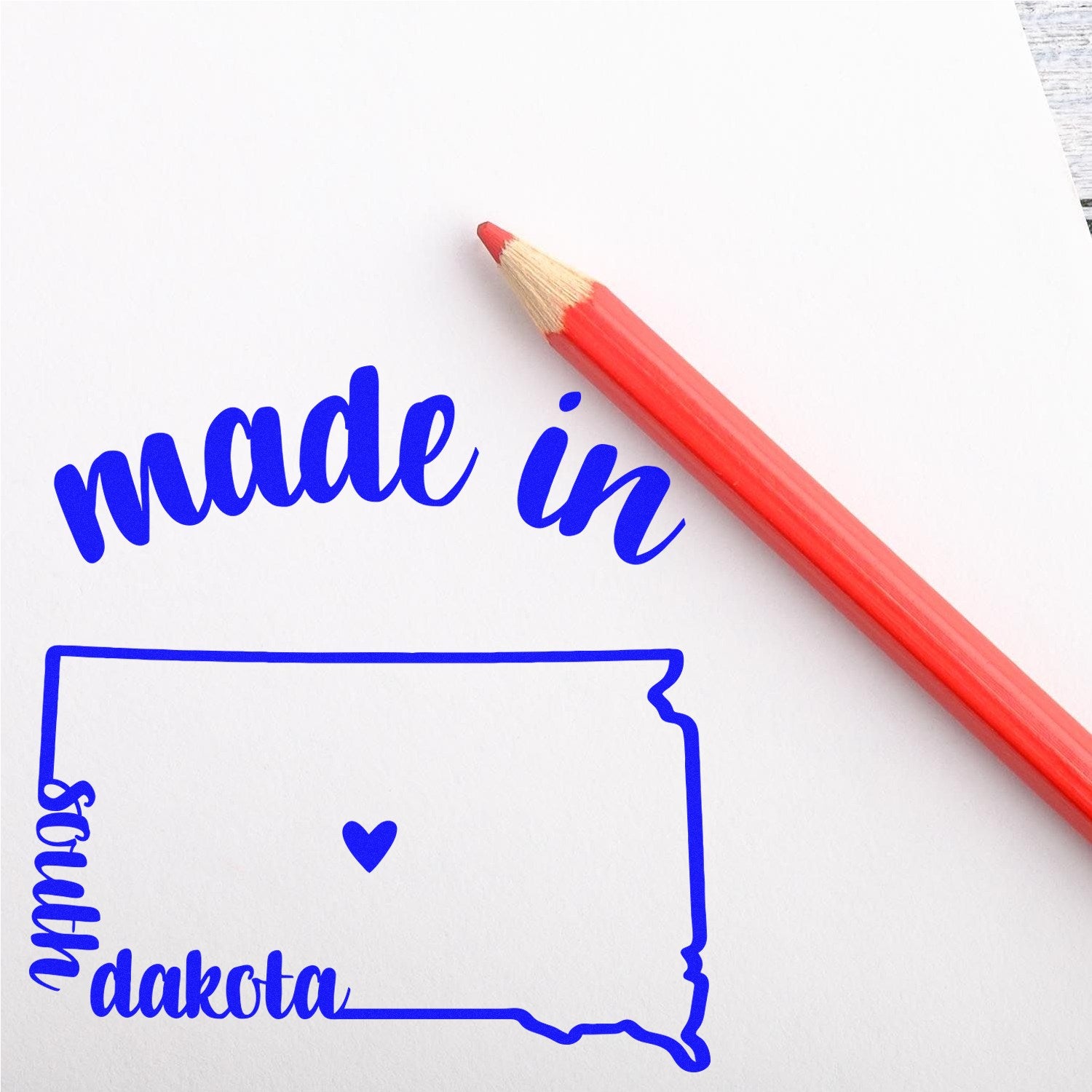 Slim Pre-Inked Stamp South Dakota Made in Stamp featuring a blue outline of South Dakota with made in text and a heart, next to a red pencil on white paper.