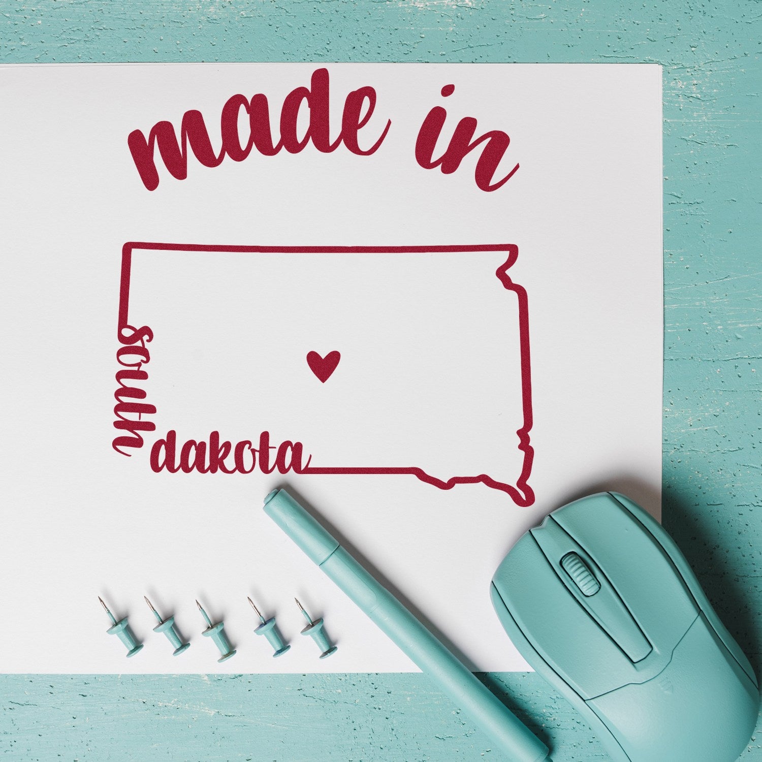 Self-Inking Handmade with Love in South Dakota Stamp on teal desk with paper, mouse, pen, and push pins. Perfect for crafts and gifts.