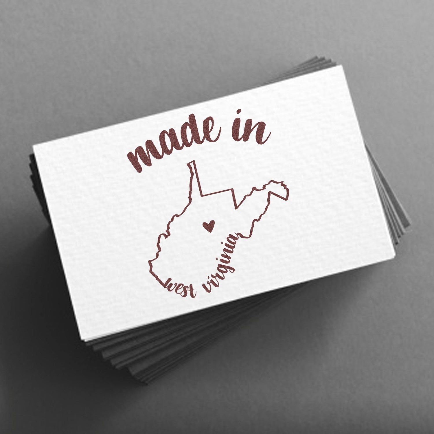 Made with Love in West Virginia Rubber Stamp featuring a heart within the state outline, perfect for crafts and gifts. High-quality design on a stack of white cards.