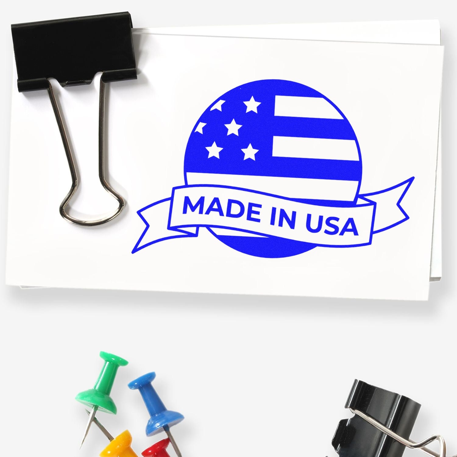 Self-Inking Patriot Seal Of Quality Stamp in use, featuring a blue Made in USA design with stars and stripes on white paper, alongside colorful push pins and a black binder clip.