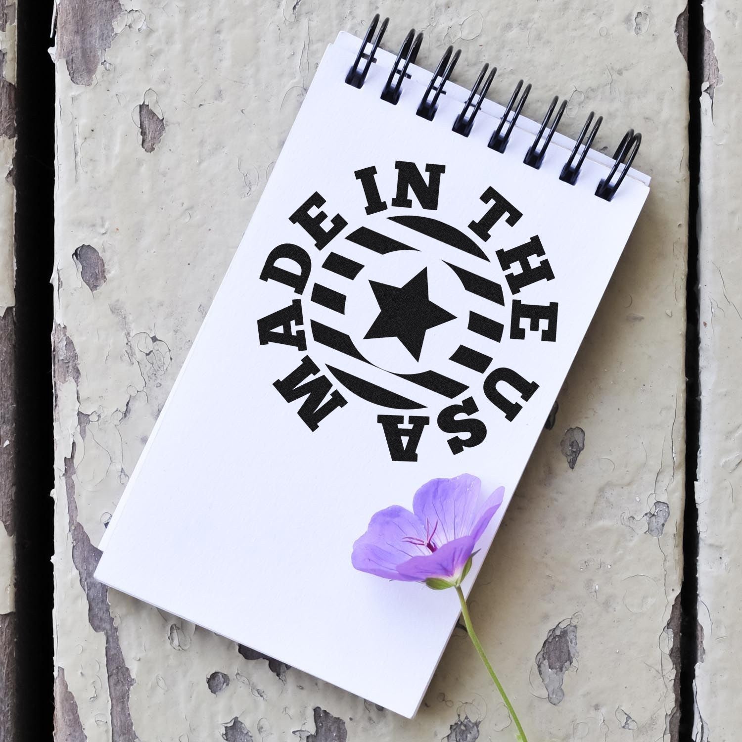 Self-Inking Made In The USA Star Emblem Stamp on a notepad with a purple flower, showcasing a bold black star design and text. Perfect for adding a patriotic touch to your projects.