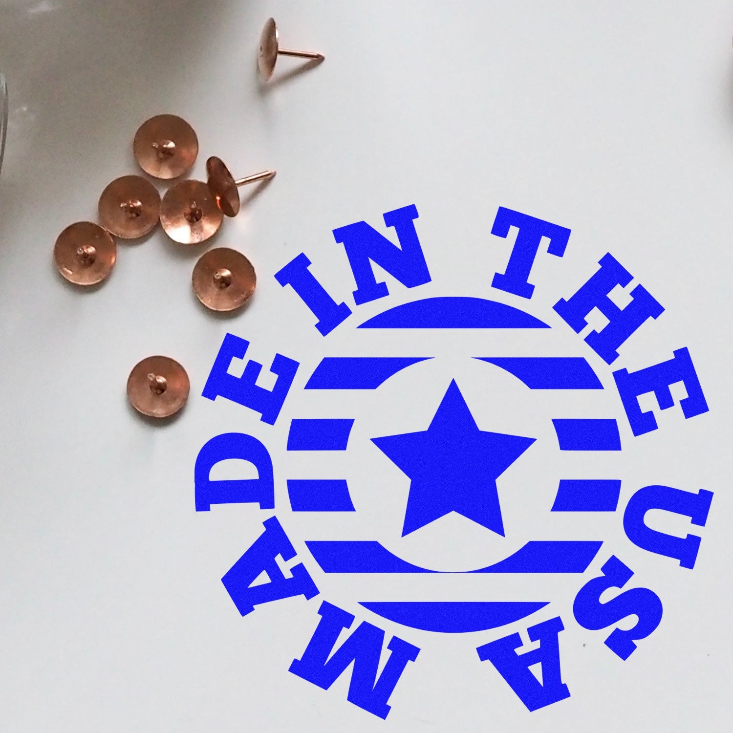 Slim Pre-Inked Made In The USA Star Emblem Stamp with blue star and stripes design, shown on a white surface with copper tacks. Perfect for crafting and office use.