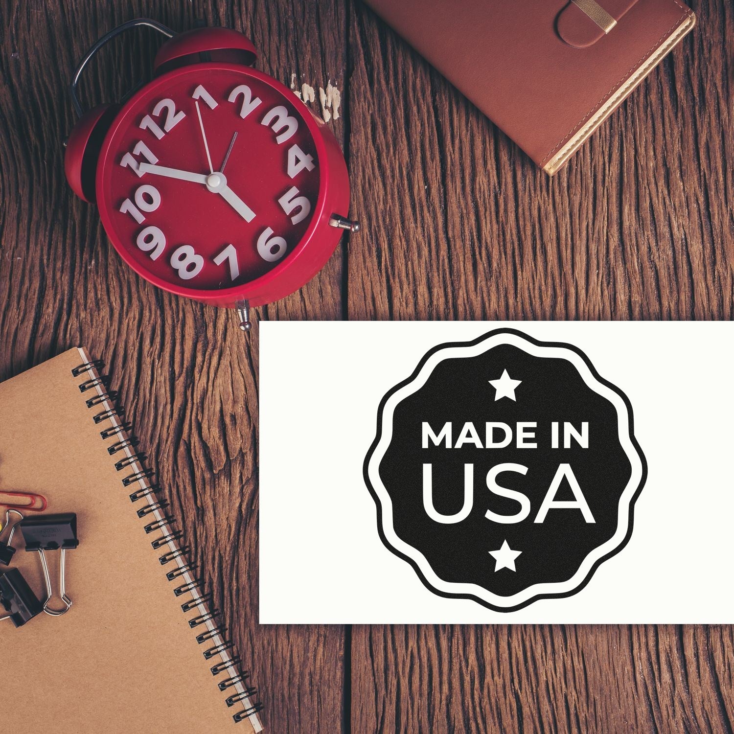 Self-Inking USA Craftsmanship Seal Stamp on a wooden desk with a red clock, notebook, and stationery, showcasing Made in USA design. Perfect for adding a professional touch to documents.