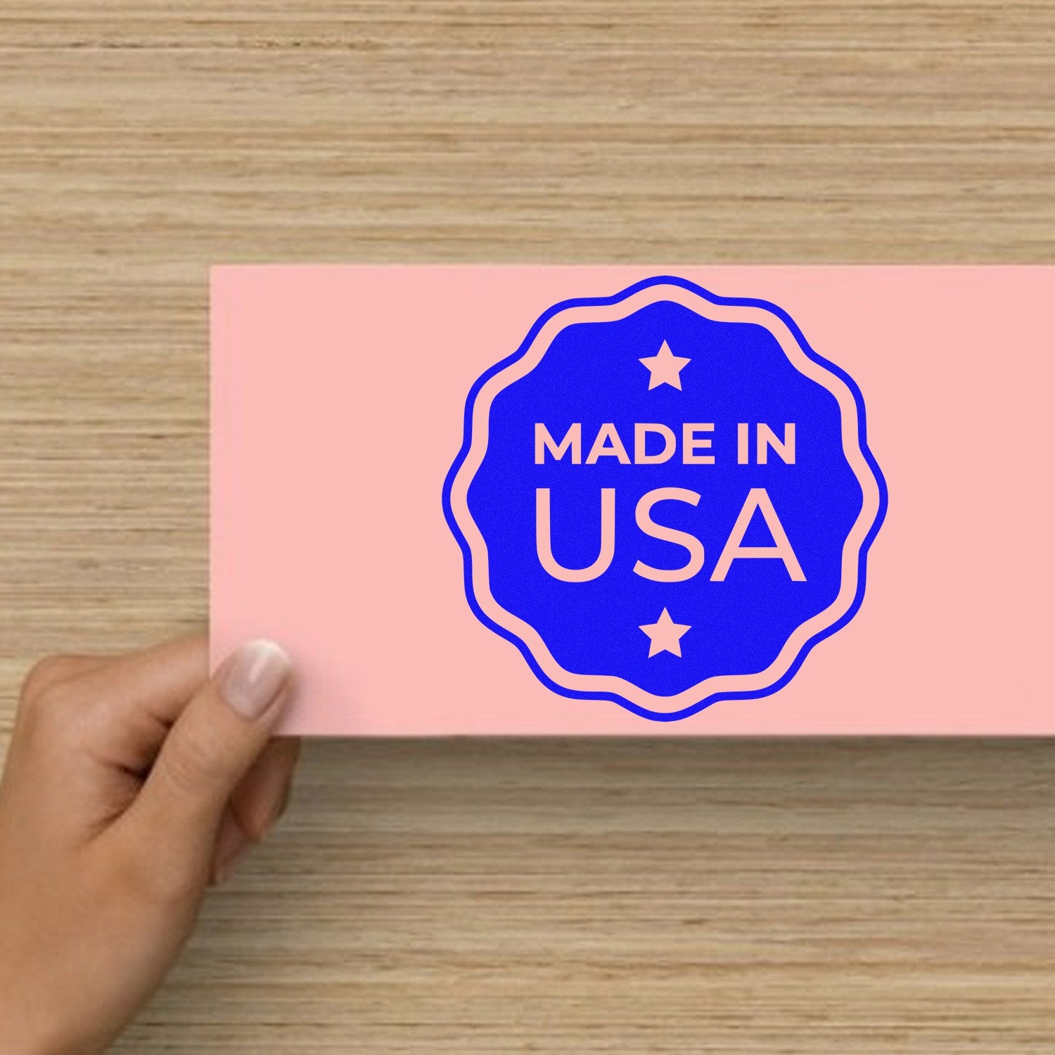 Self-Inking USA Craftsmanship Seal Stamp in use, featuring a blue Made in USA design on a pink card, held by a hand. Perfect for adding a professional touch to your projects.