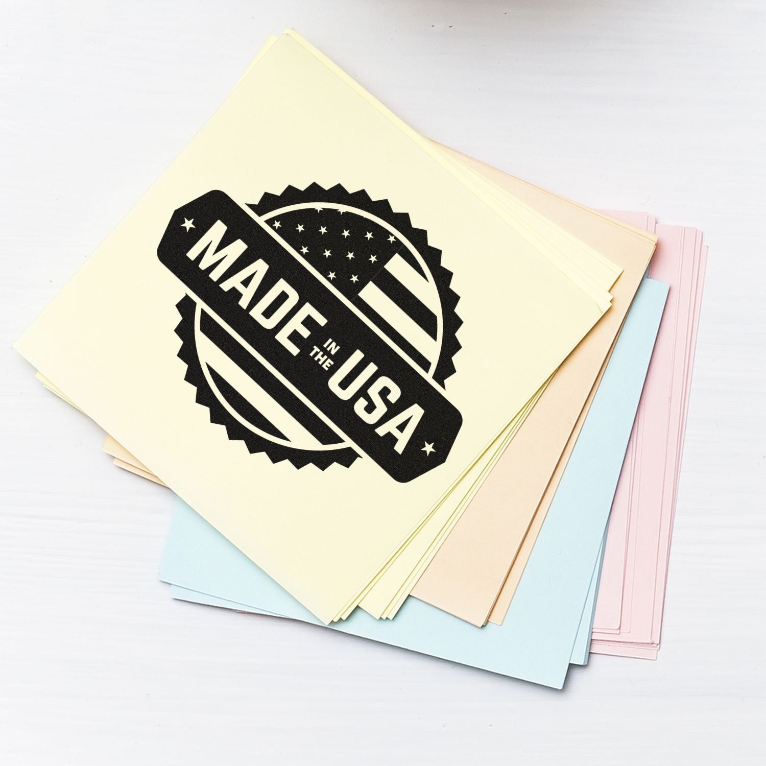 Self-Inking American Craftsmanship Seal Stamp on pastel paper stack, featuring Made in the USA design with stars and stripes. Perfect for adding a patriotic touch to crafts and documents.