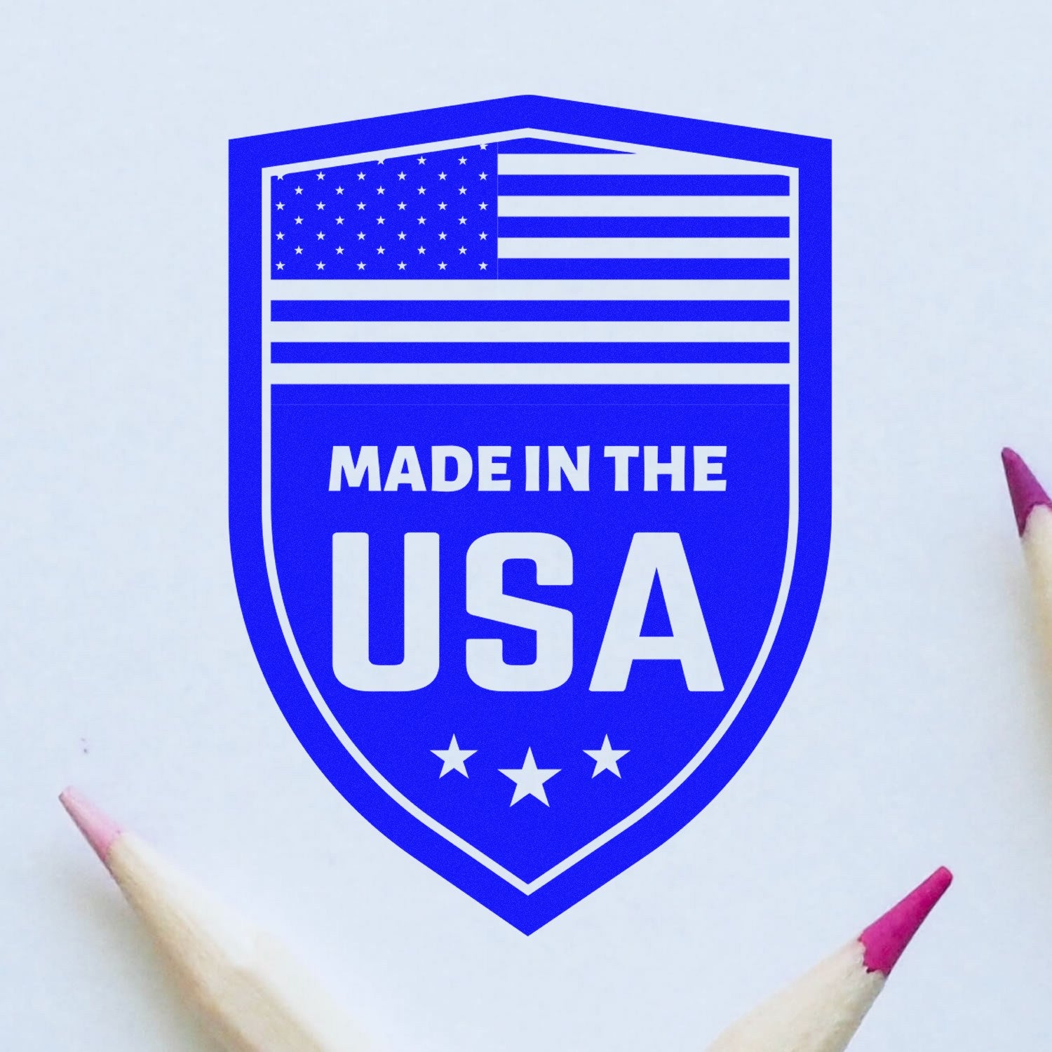 Self-Inking Proudly Made In The USA Stamp with blue shield design, American flag, and bold text, surrounded by pencils on a white background.