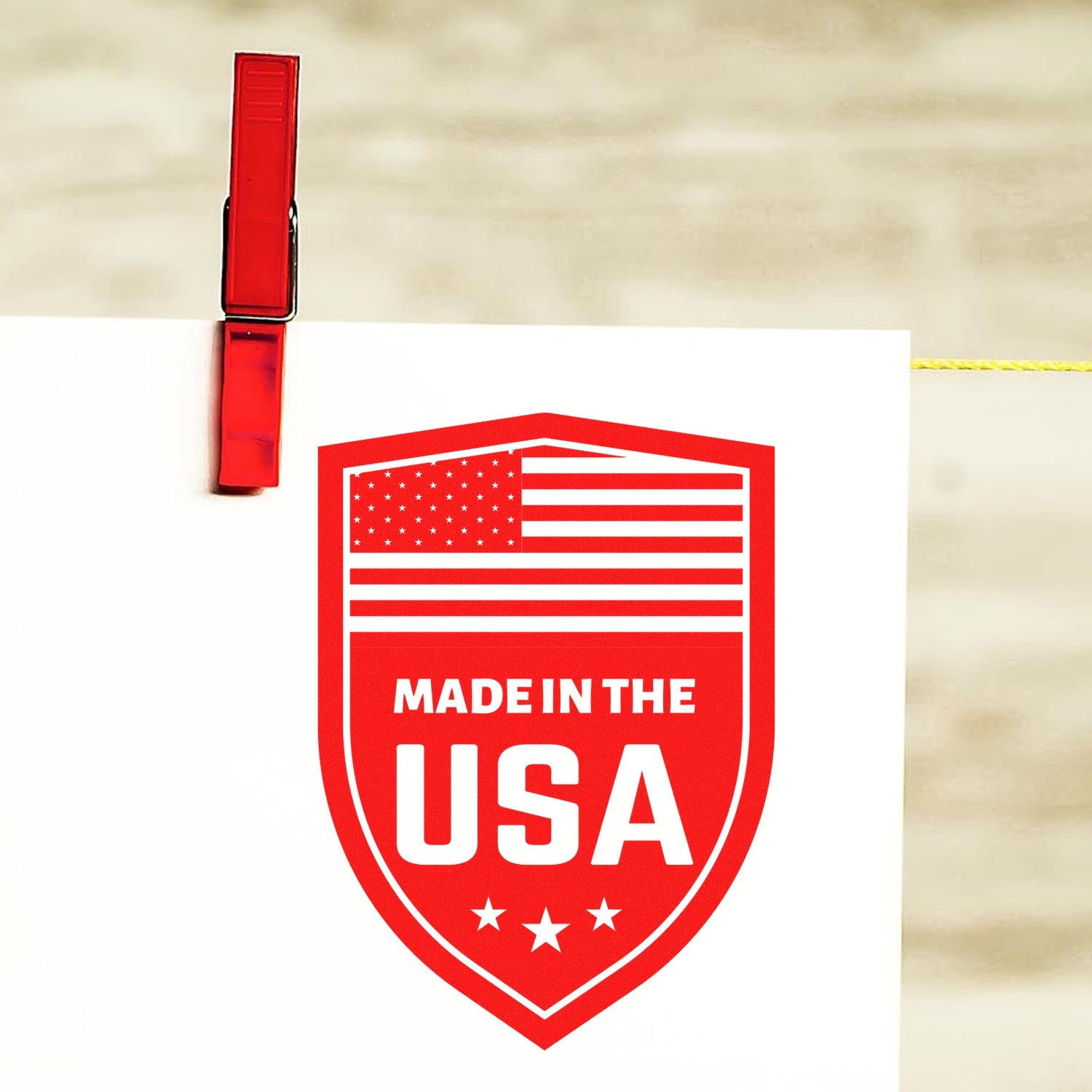 Self-Inking Proudly Made In The USA Stamp with red and white design, featuring an American flag and stars, clipped to a line. Perfect for adding a patriotic touch to documents and crafts.