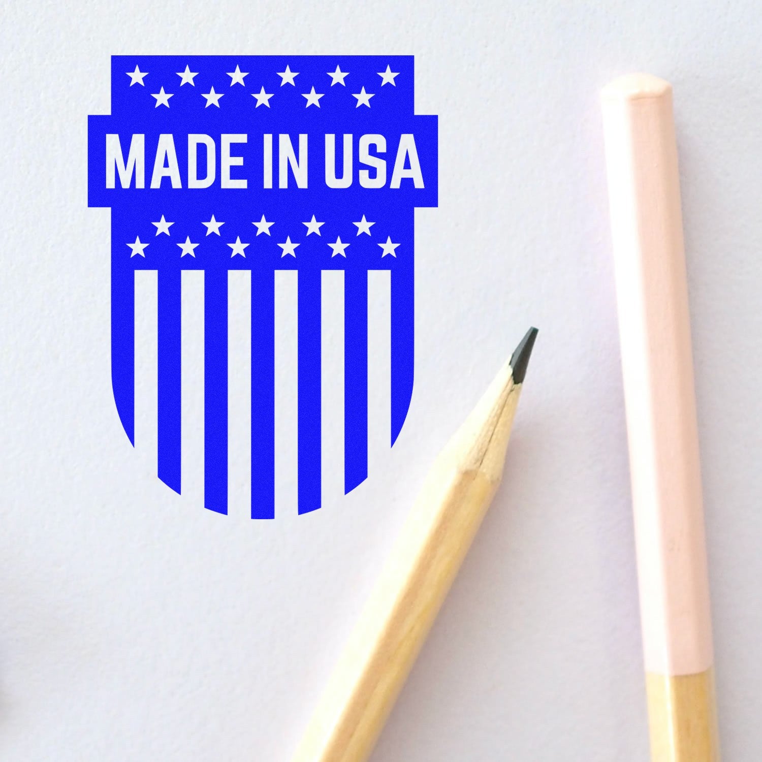 Slim Pre-Inked Patriotic Emblem Stamp featuring a blue Made in USA design with stars and stripes, shown next to a pencil on a light background. Perfect for adding a patriotic touch.