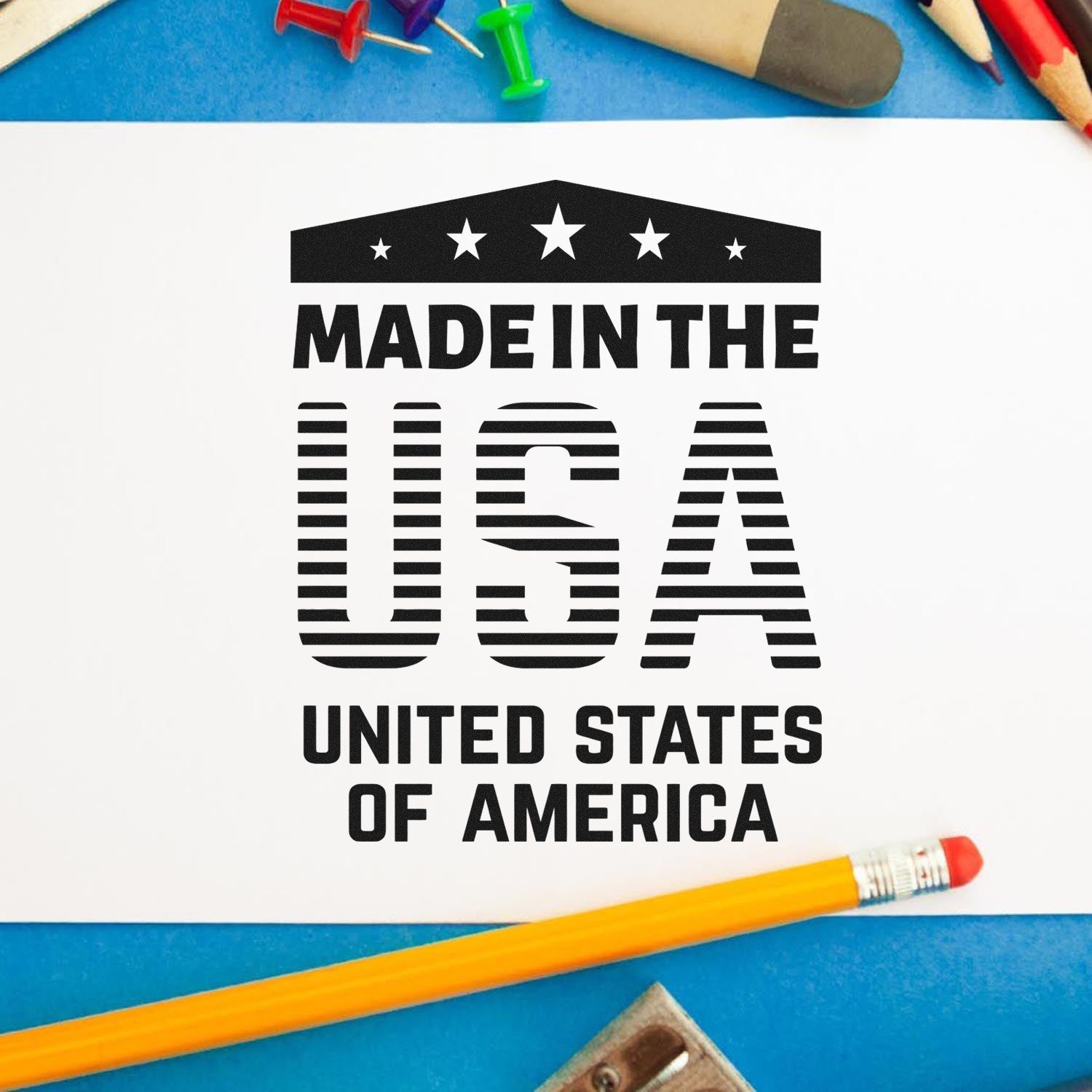 Image of the Slim Pre-Inked Patriotic Pride Stamp imprinting Made in the USA on paper, surrounded by colorful push pins and a pencil, showcasing its crisp, bold design.