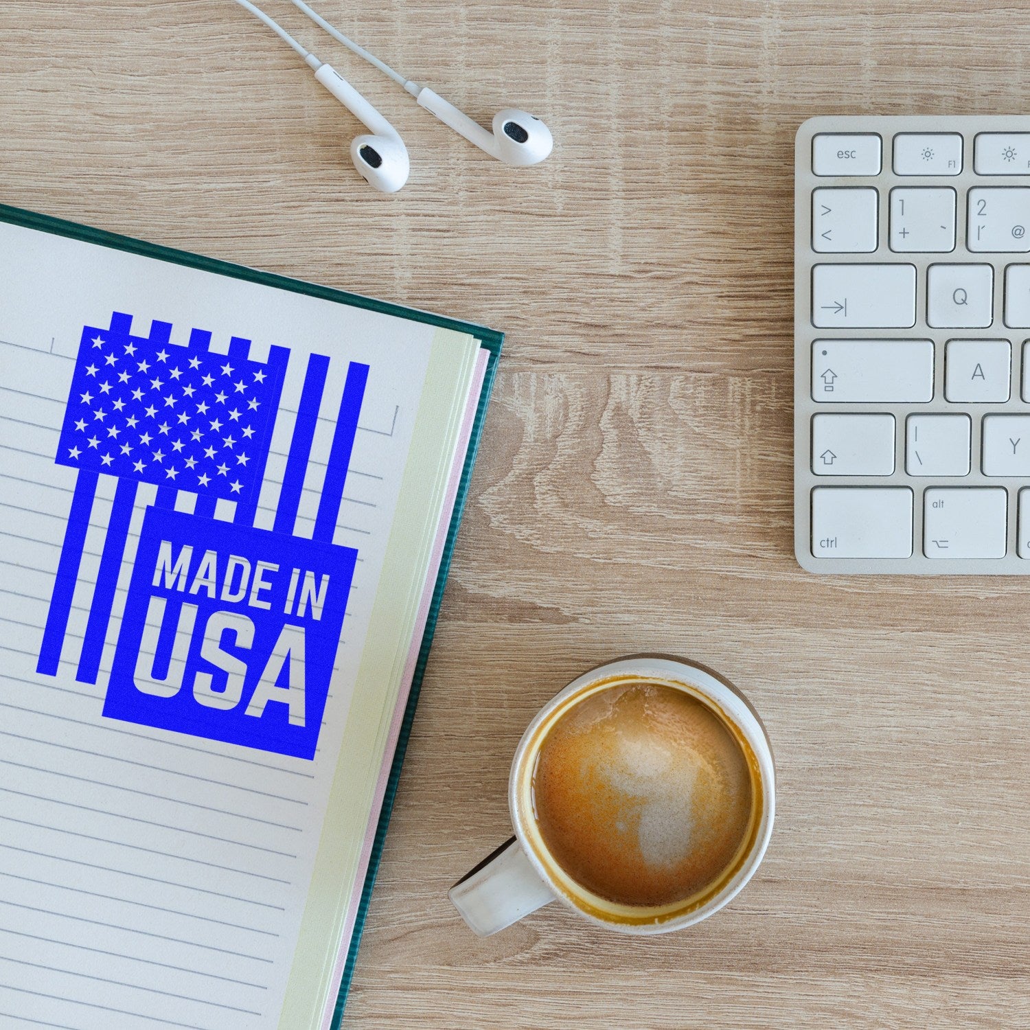 Wood Handle USA Patriotic Pride Rubber Stamp on a notebook, featuring a blue 'Made in USA' design with stars and stripes, next to a coffee cup, keyboard, and earphones.