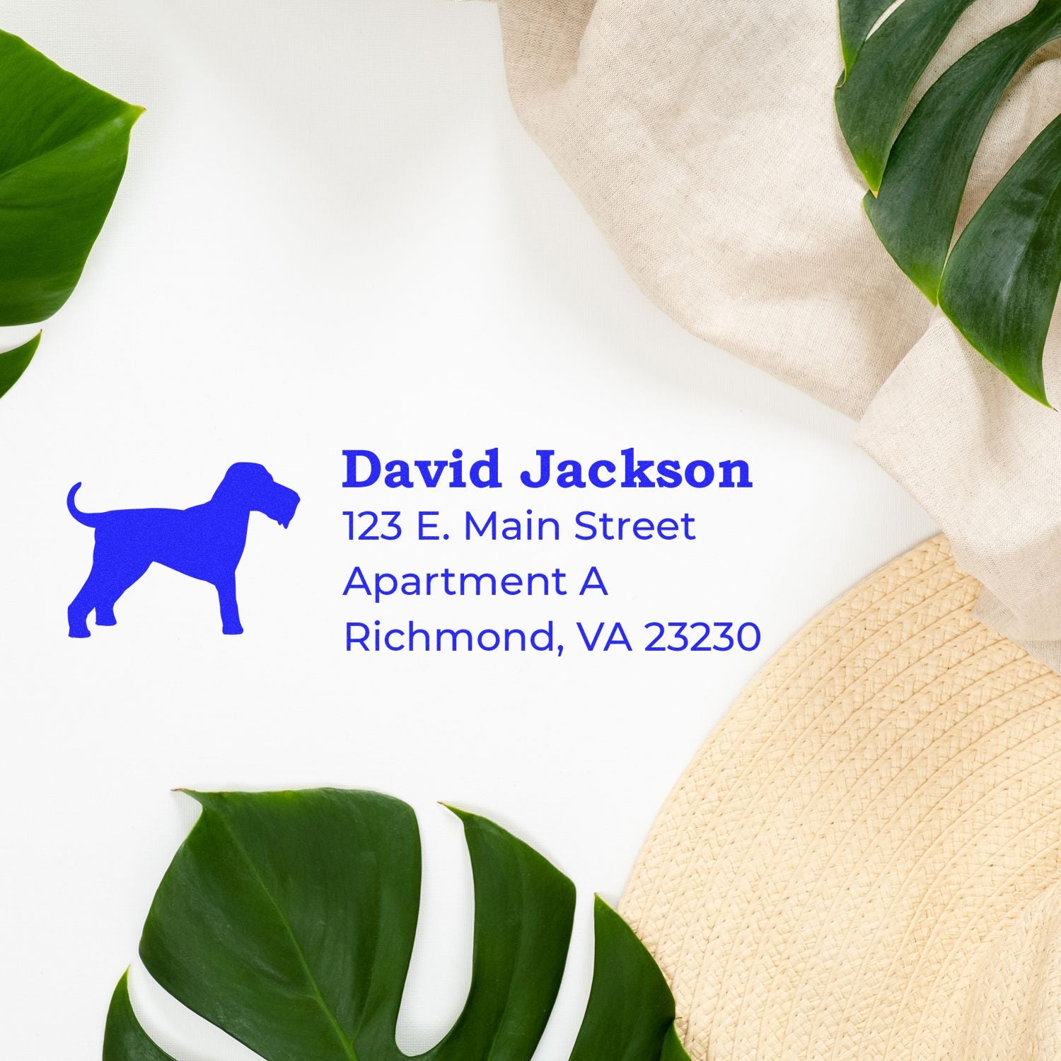 PSI Pre-Inked Personalized Airedale Terrier Address Stamp on white paper with blue text, featuring a dog silhouette. Surrounded by green leaves and a beige hat for a stylish presentation.