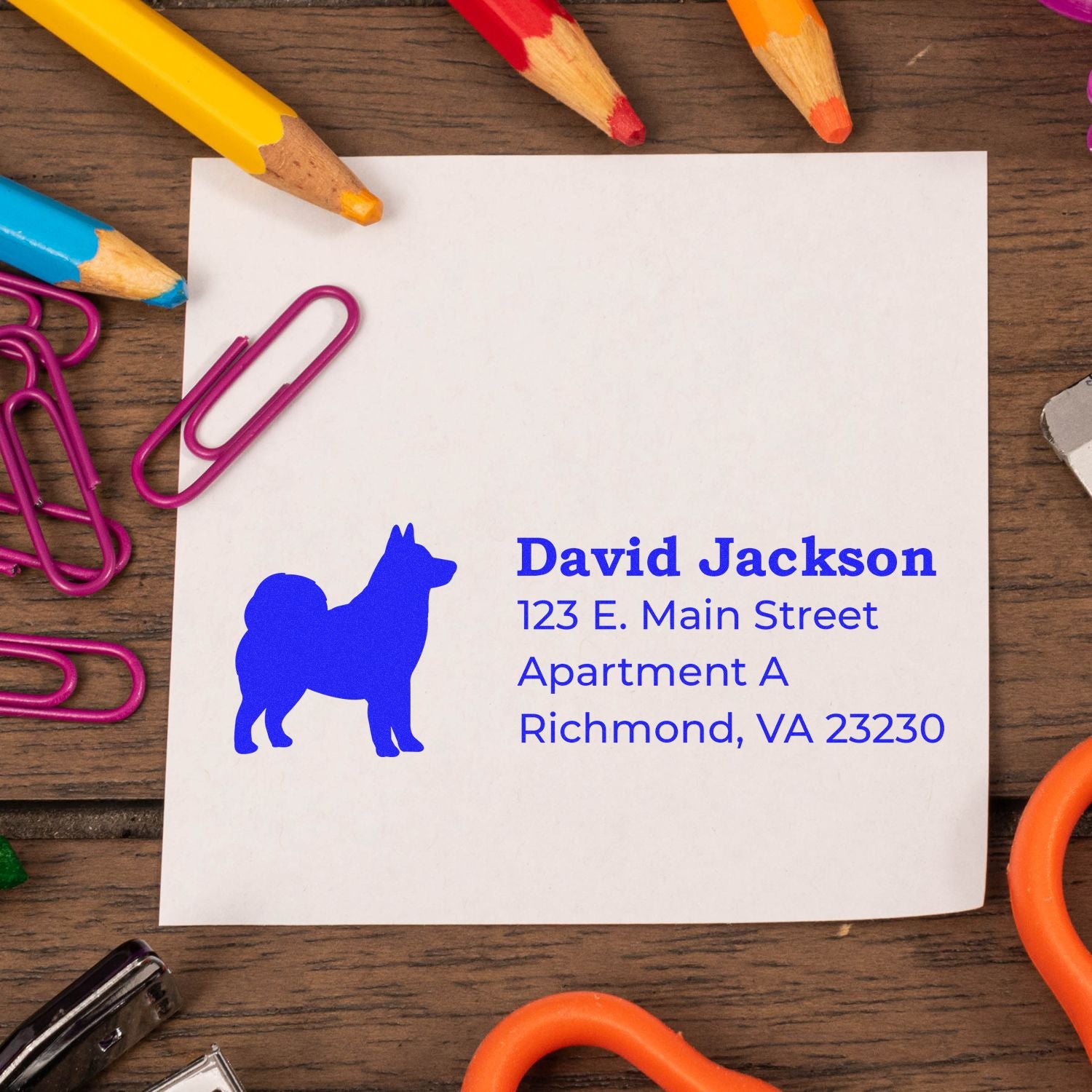 Self-Inking Alaskan Malamute Dog Address Stamp on paper with colorful pencils and paperclips on a wooden desk.