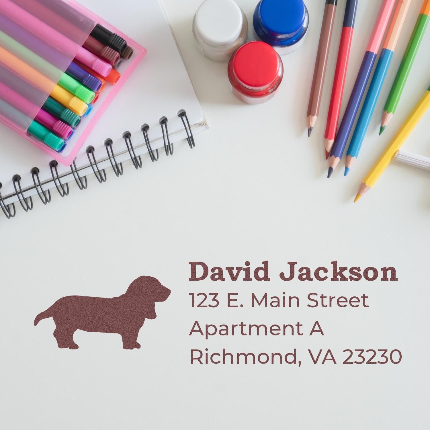 Basset Hound Silhouette Address Rubber Stamp on paper with colorful pens, pencils, and paint jars nearby. The stamp displays a basset hound silhouette and an address in a stylish font.