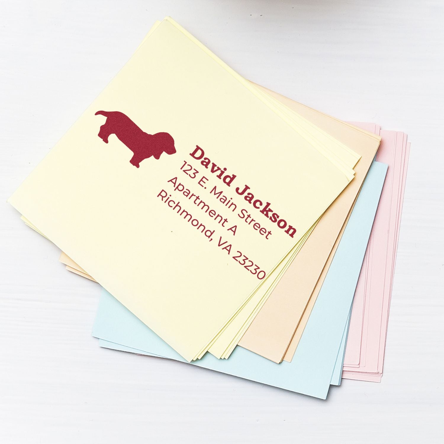 Slim Pre-Inked Basset Hound Address Stamp on pastel envelopes, featuring a red basset hound silhouette and sample address text. Perfect for adding a personal touch to your mail.