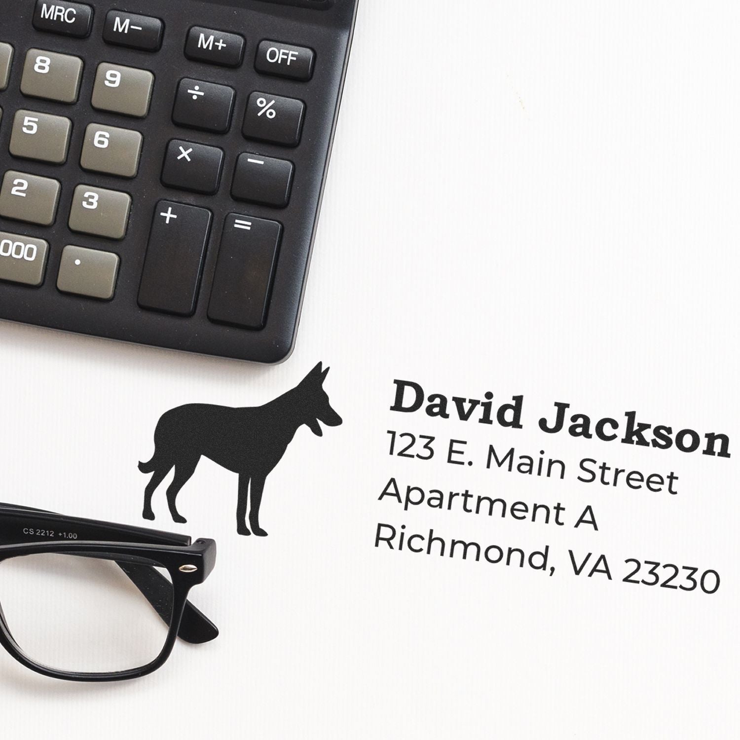 Self-Inking Belgian Malinois Dog Address Stamp on paper with a silhouette of the dog, next to a calculator and glasses, showcasing a sample address in bold, clear font.