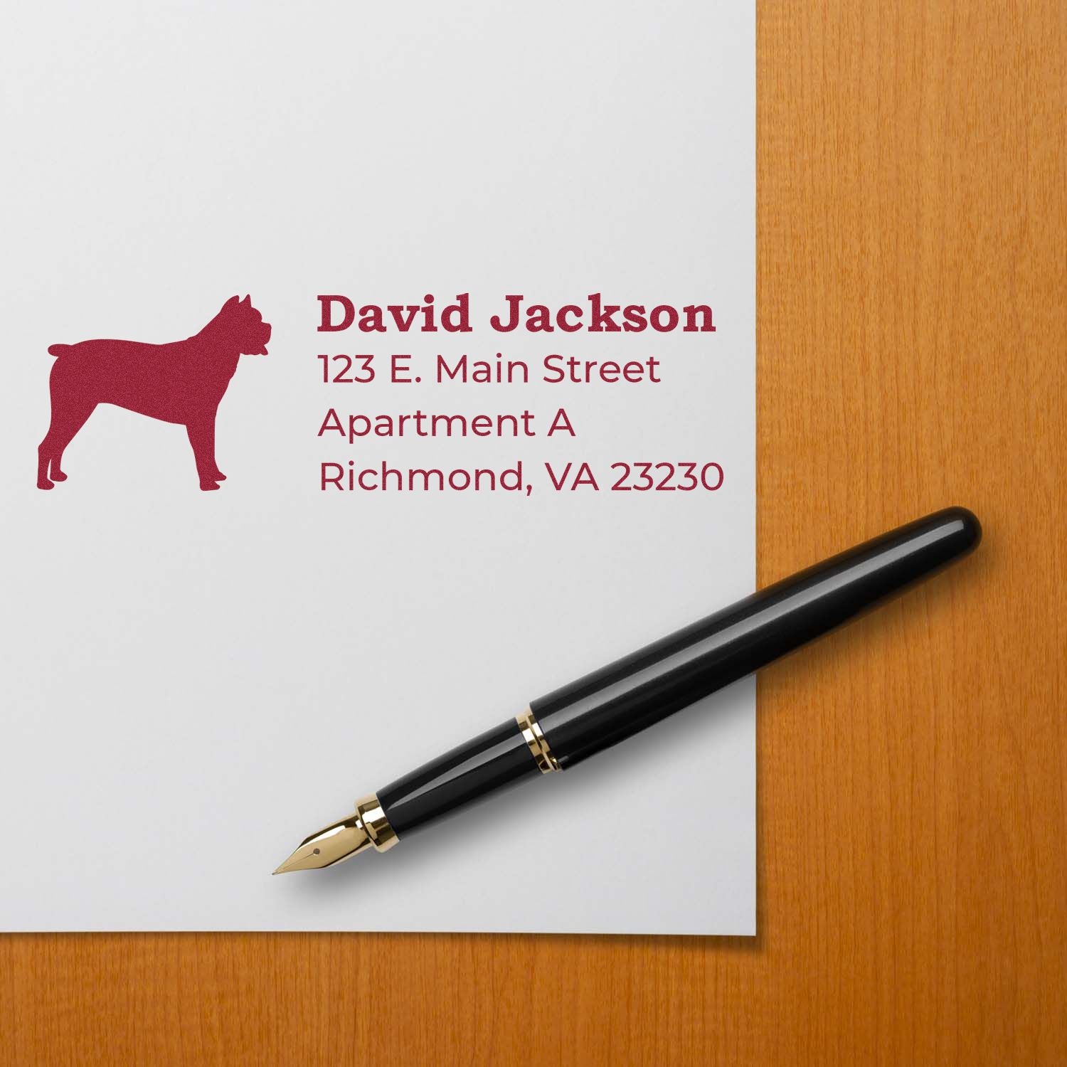 Cane Corso Silhouette Address Rubber Stamp on paper with a red dog silhouette and address details. A black fountain pen rests nearby on a wooden surface.